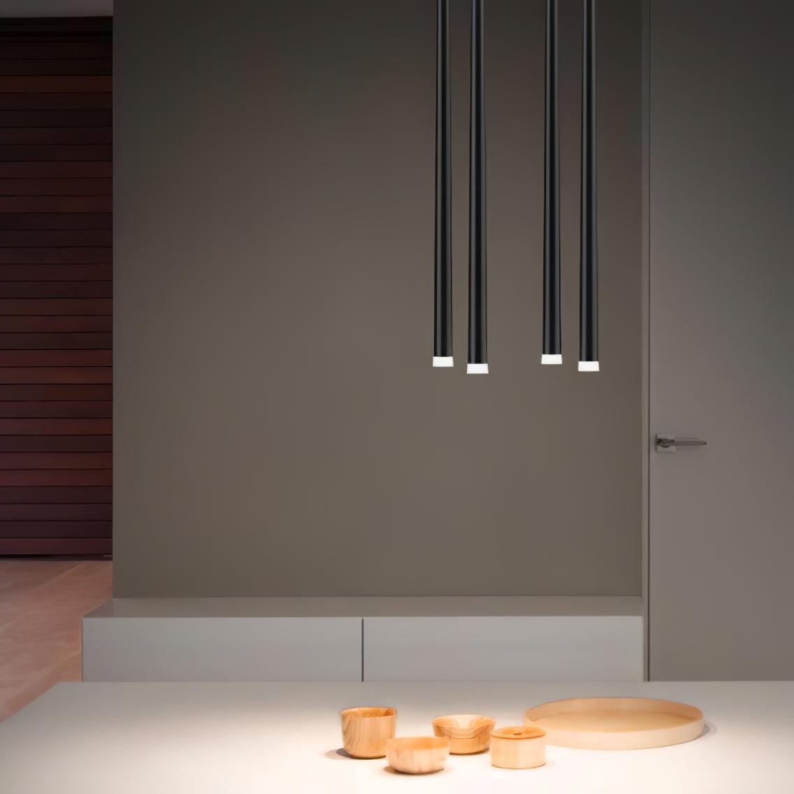 Four black pendant tubes above a white table with wooden bowls, with the upper cables cropped