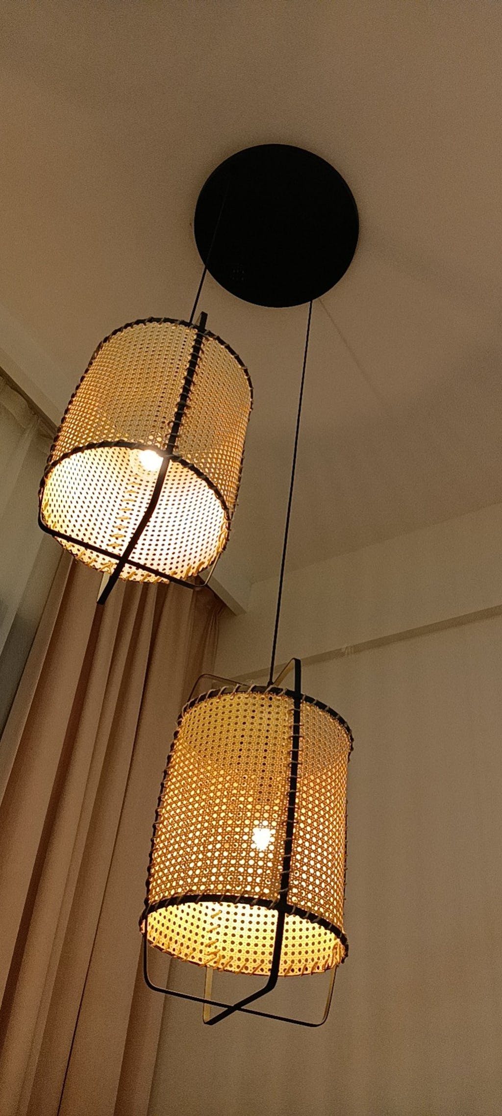 Low angle of two glowing cane pendants on a shared round black canopy, with open bottoms and visible bulbs