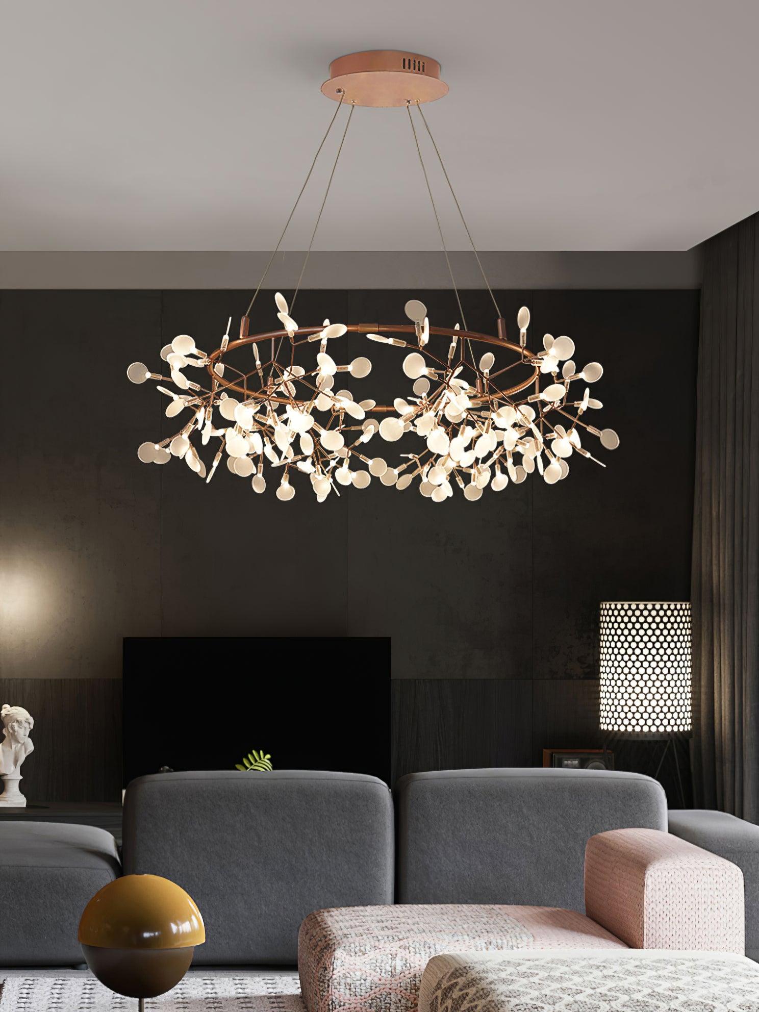 Warm metallic leaf ring chandelier above grey lounge chairs, a pale ottoman and a yellow spherical side object