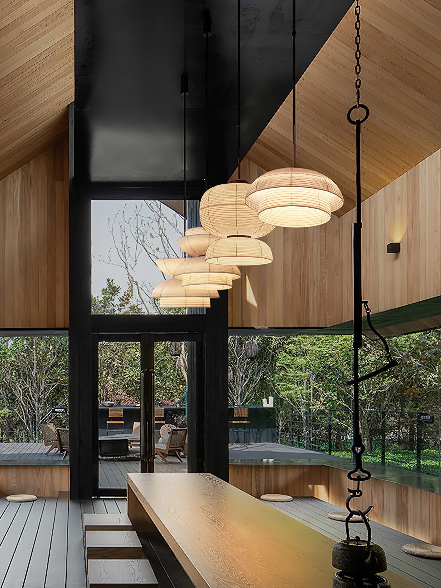 Portrait row of varied fabric pendants above a long wood table under a pitched roof, beside garden-facing glazing