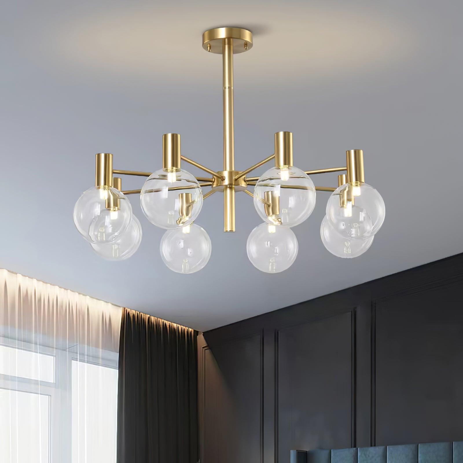 Low angled close view of eight clear globes and lit capsule lamps on gold-tone arms beside a sheer curtain.