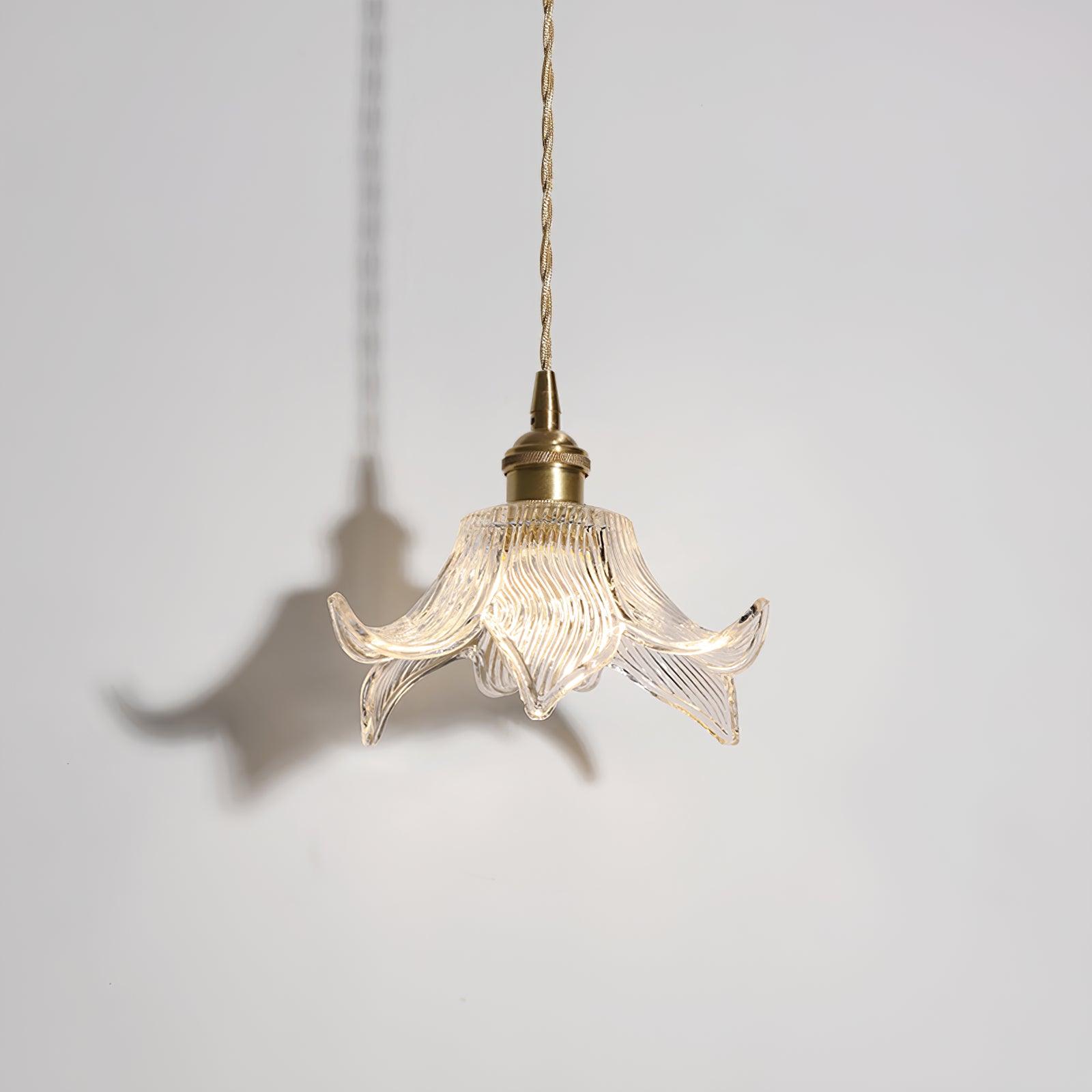 Unlit ribbed glass pendant against a white wall with a flower-shaped shadow cast to the left.