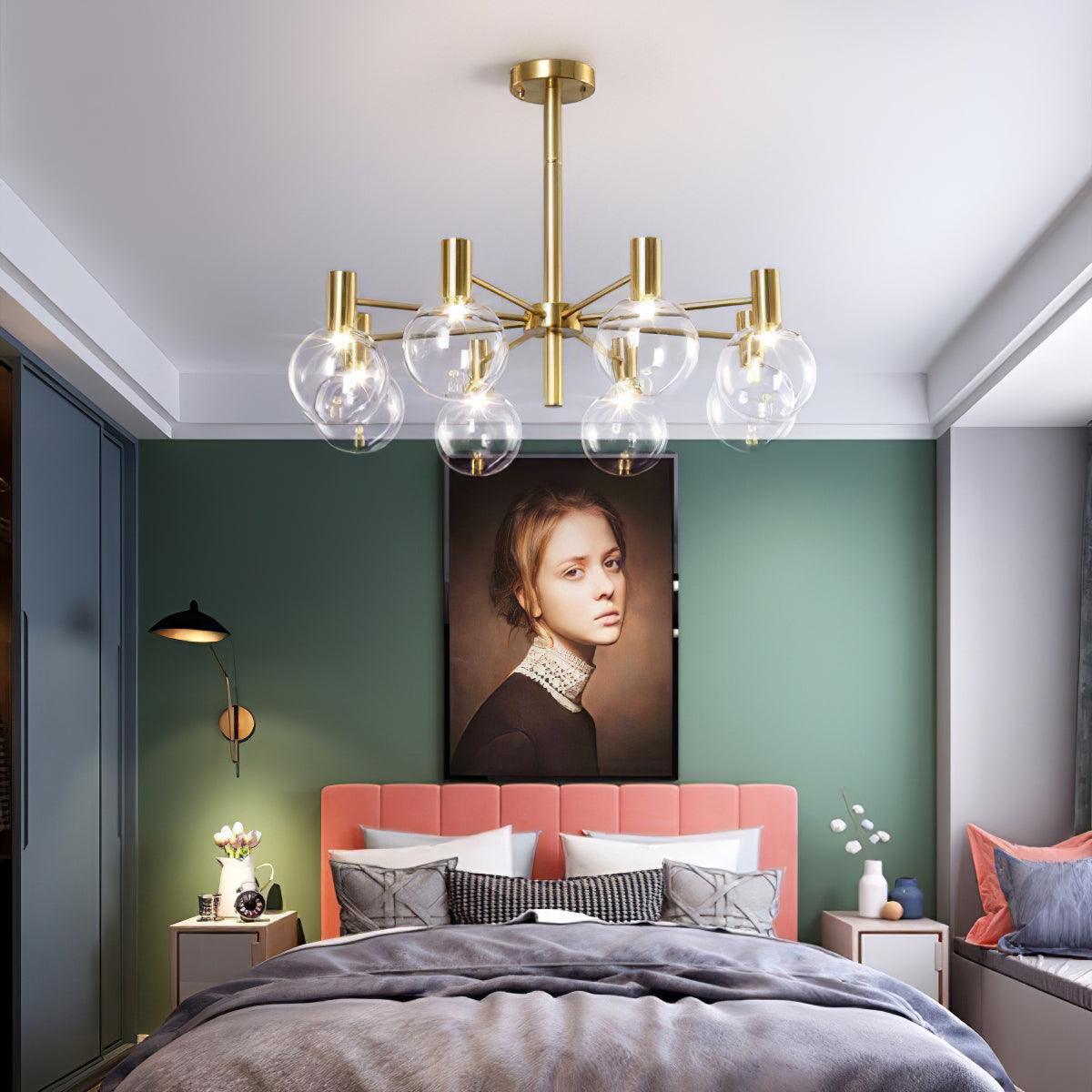 Eight-clear-globe chandelier above a bed with a pink headboard, grey bedding and portrait artwork on a green wall.