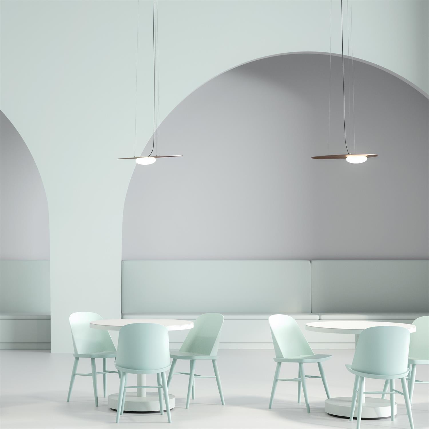 Two thin gold-tone pendants above round white tables and mint chairs, with arched wall shapes and pale bench seating.