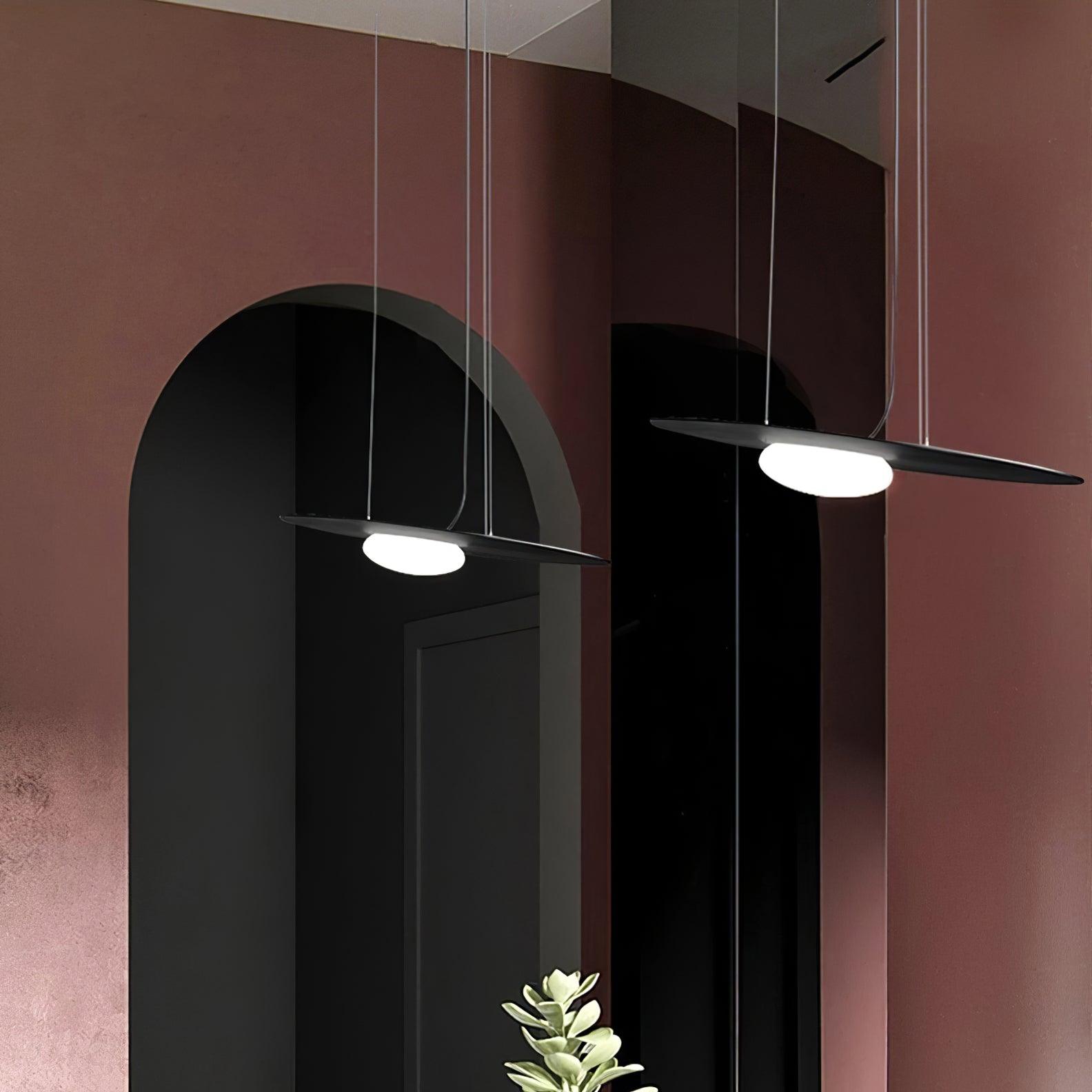 Two black disc pendants at staggered heights against rose walls and dark arched recesses, with green foliage below.