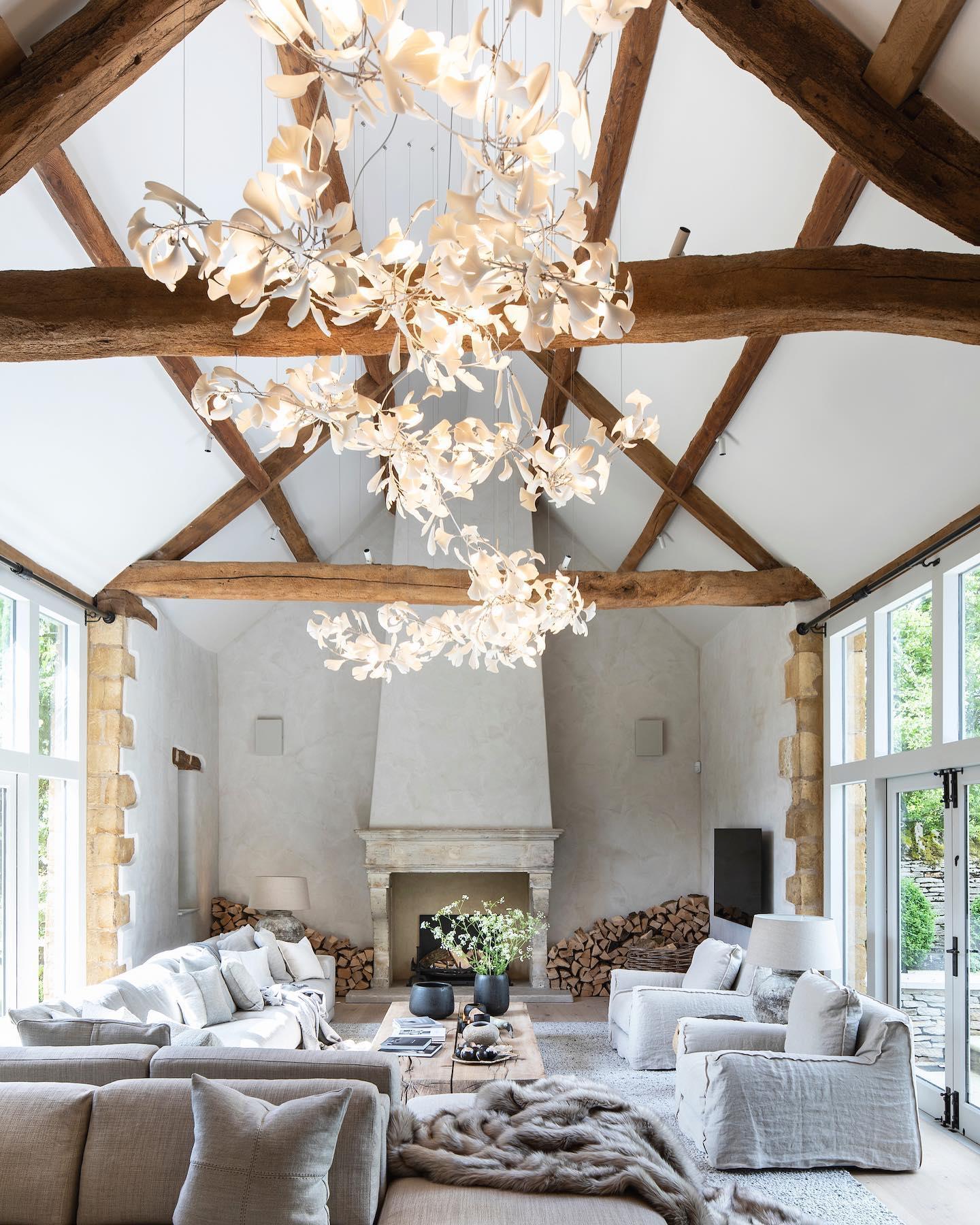Cascading white ginkgo leaf installation in a tall timber-beamed room above pale seating and a fireplace