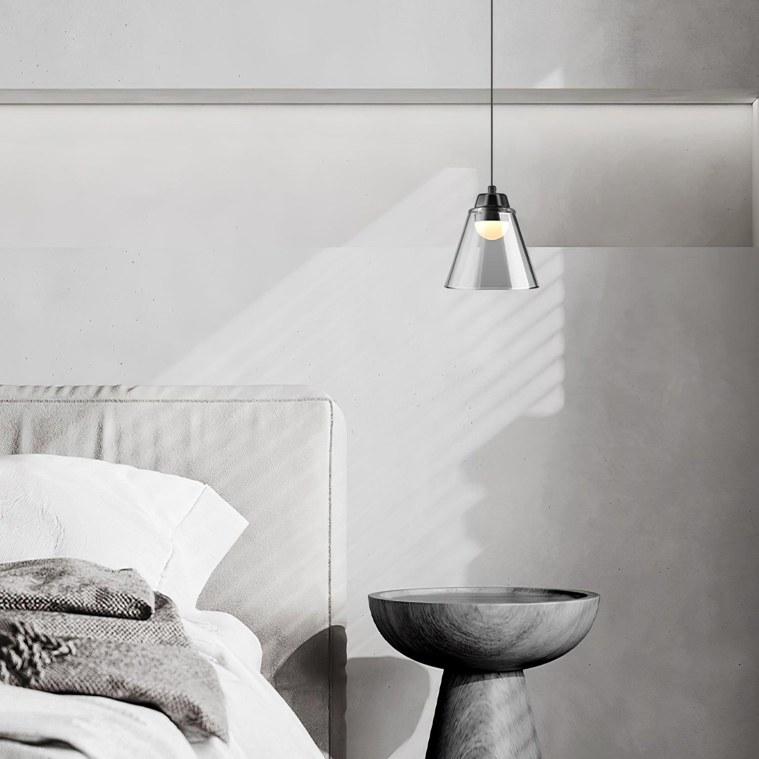 Single glass cone pendant beside a bed and dark table