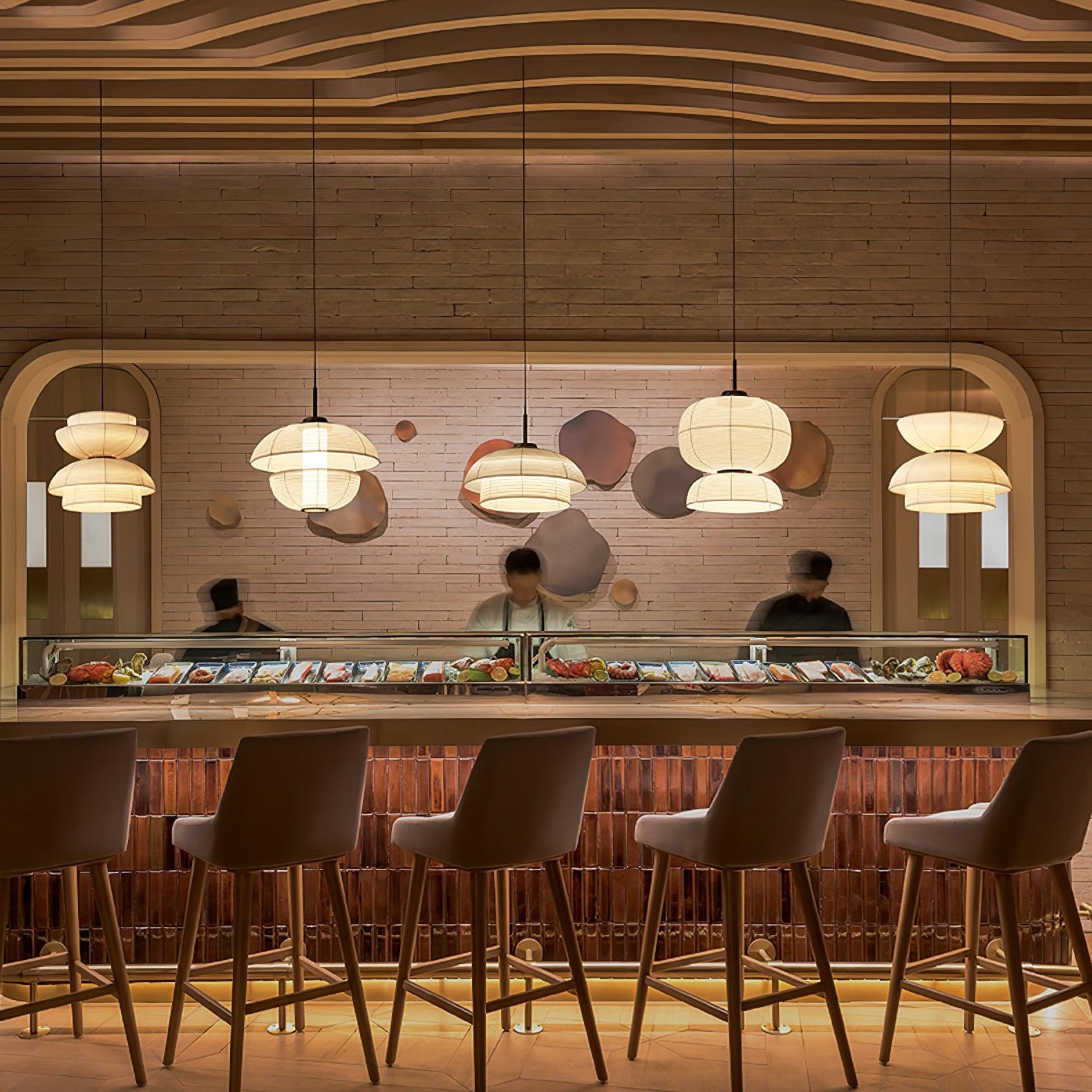 Five separate fabric pendants in varied shapes above a restaurant counter with barstools