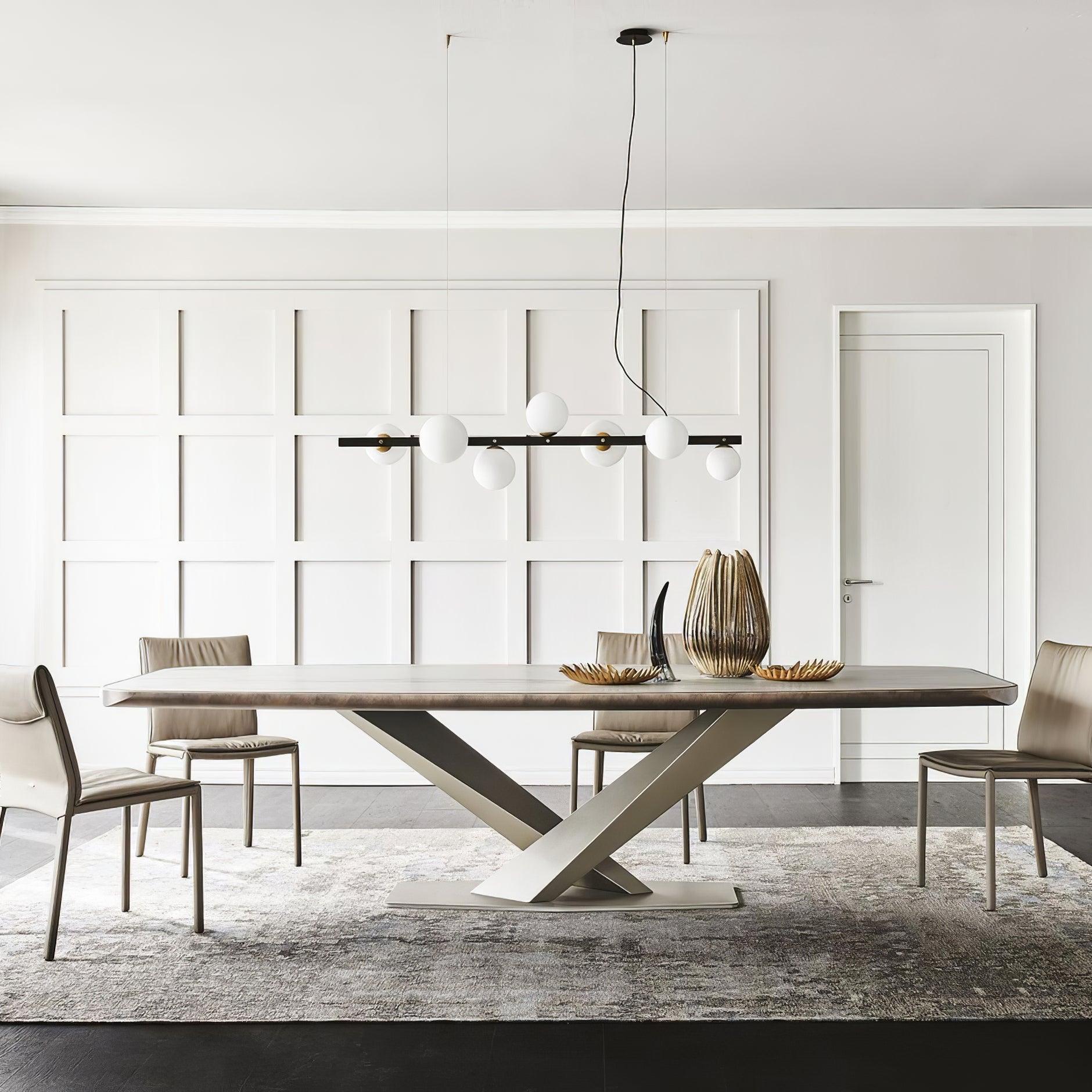 Wide dining view of globe pendant and separate round canopy above pale table, beige chairs, ribbed gold-tone vase and leaf dishes.