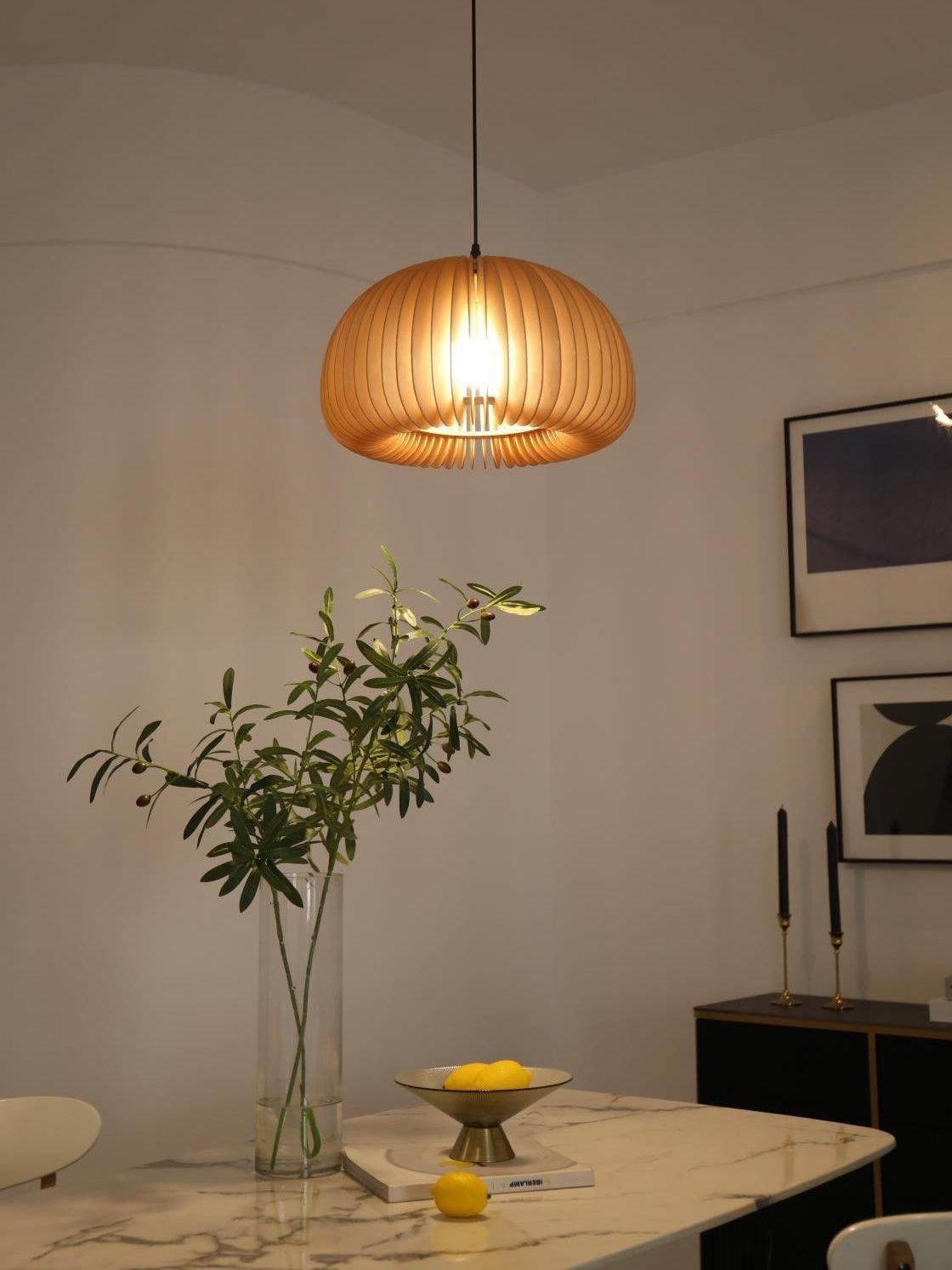 Wood slat pendant above a marble-look table with lemons and a leafy vase, near framed art and candlesticks