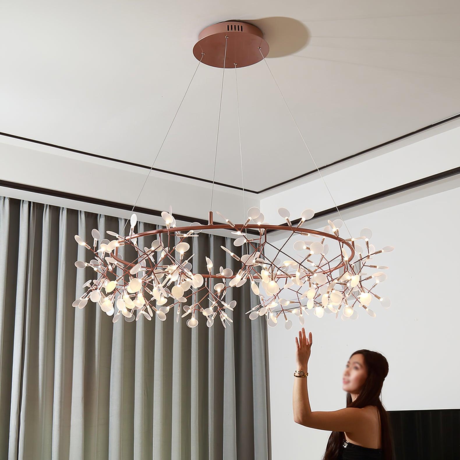 Rose-copper leaf ring chandelier with a woman reaching toward a lower leaf beside grey curtains