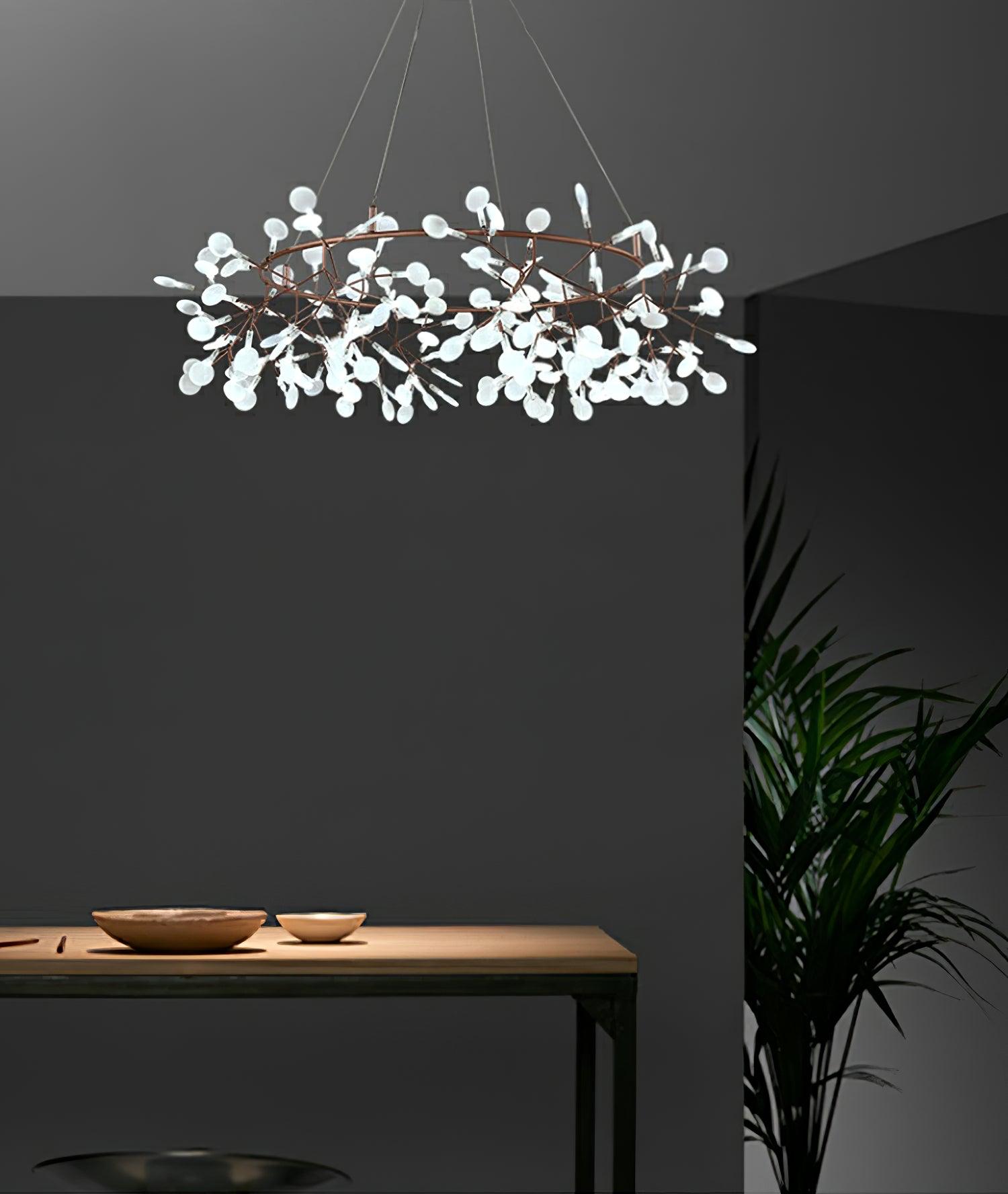 White leaf ring chandelier above a timber table with shallow bowls beside a dark wall and tall palm