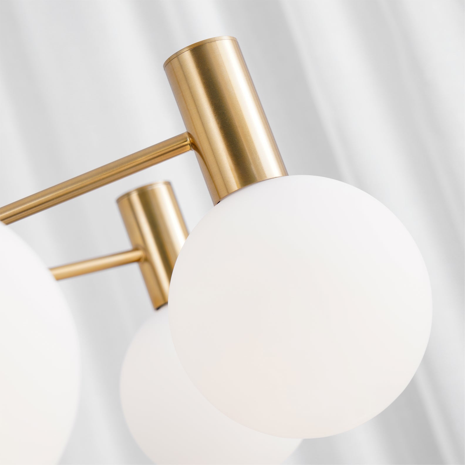 Close view of an opaque white globe beneath a gold-tone cylindrical holder, joined to a narrow metal arm.