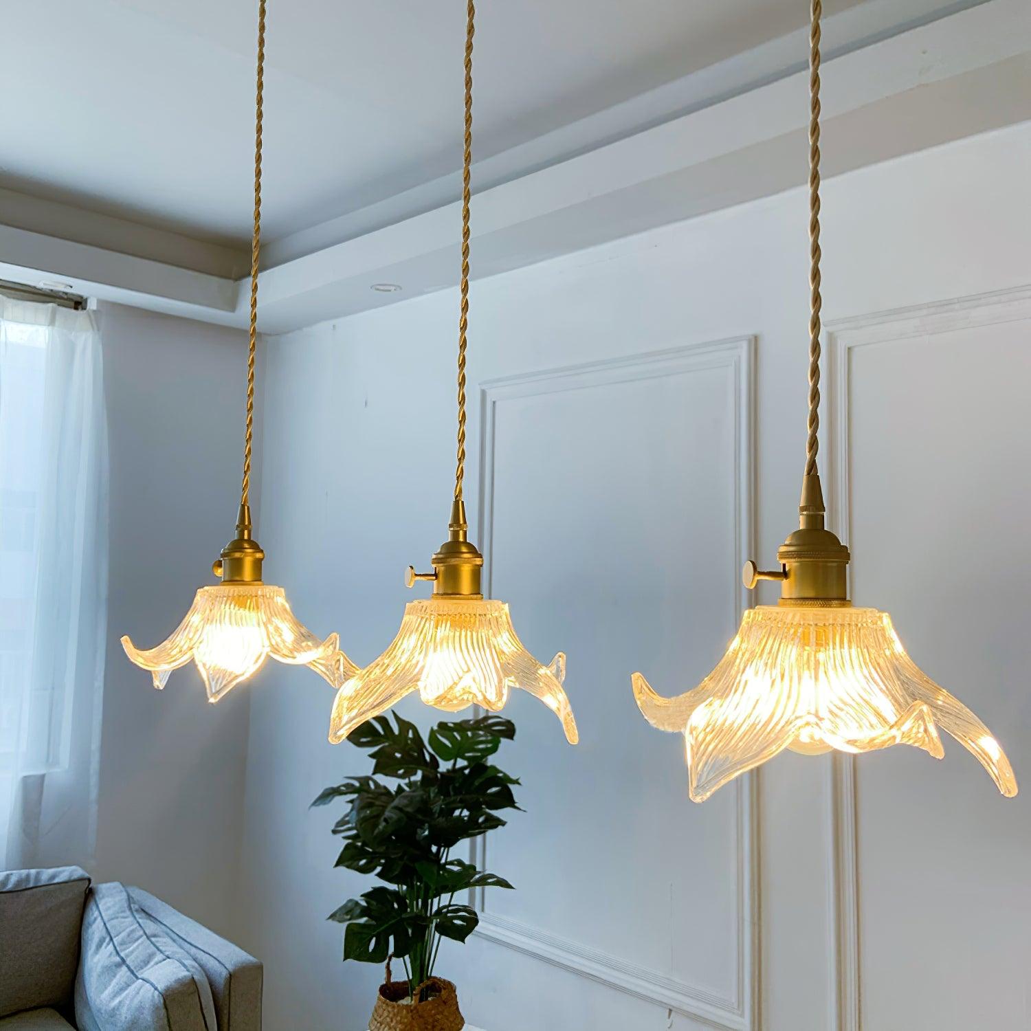 Three illuminated petal glass pendants at staggered heights near a grey sofa and a monstera in a woven basket.