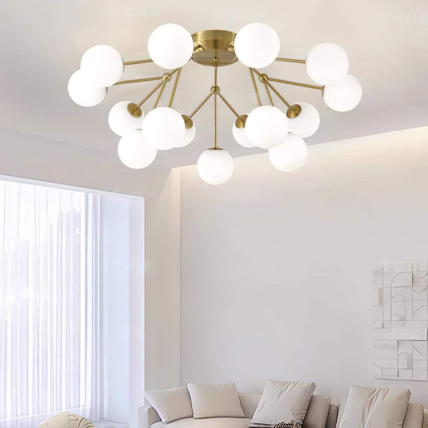 Gold globe-cluster ceiling light above a white sofa and geometric wall artwork beside sheer curtains