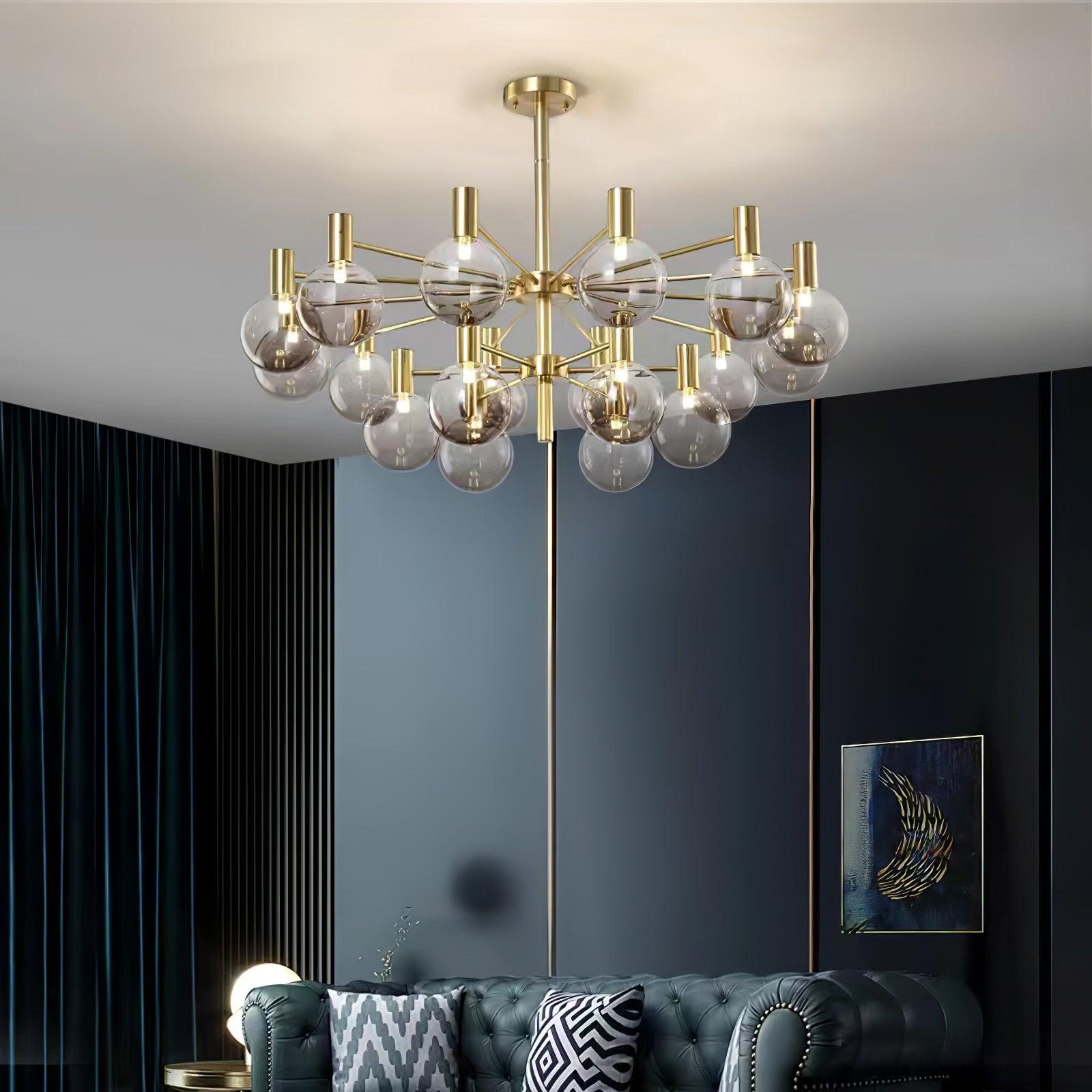 Two-tier clear-globe chandelier above a dark tufted leather sofa and patterned cushions, beside blue-grey panels and slats.