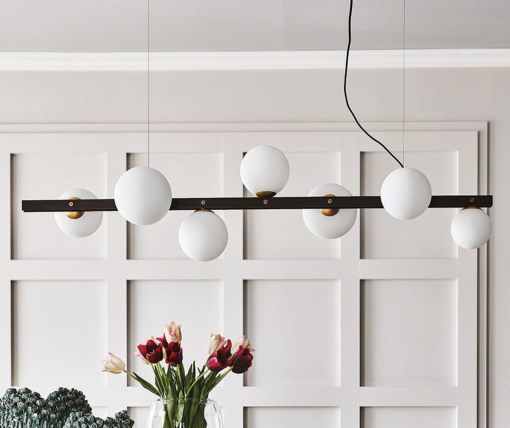 Closer unlit front view of seven globes along black bar, above red and pale tulips and green bowls against white panelling.
