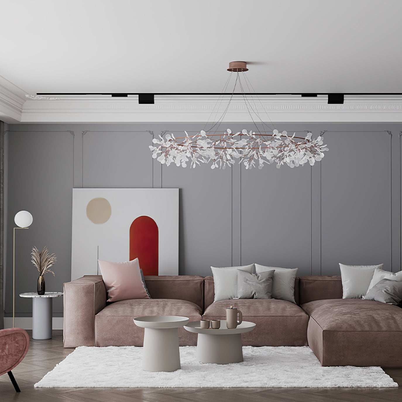 Wide rose-copper leaf ring chandelier above a taupe sofa and round white tables beside red-arch artwork