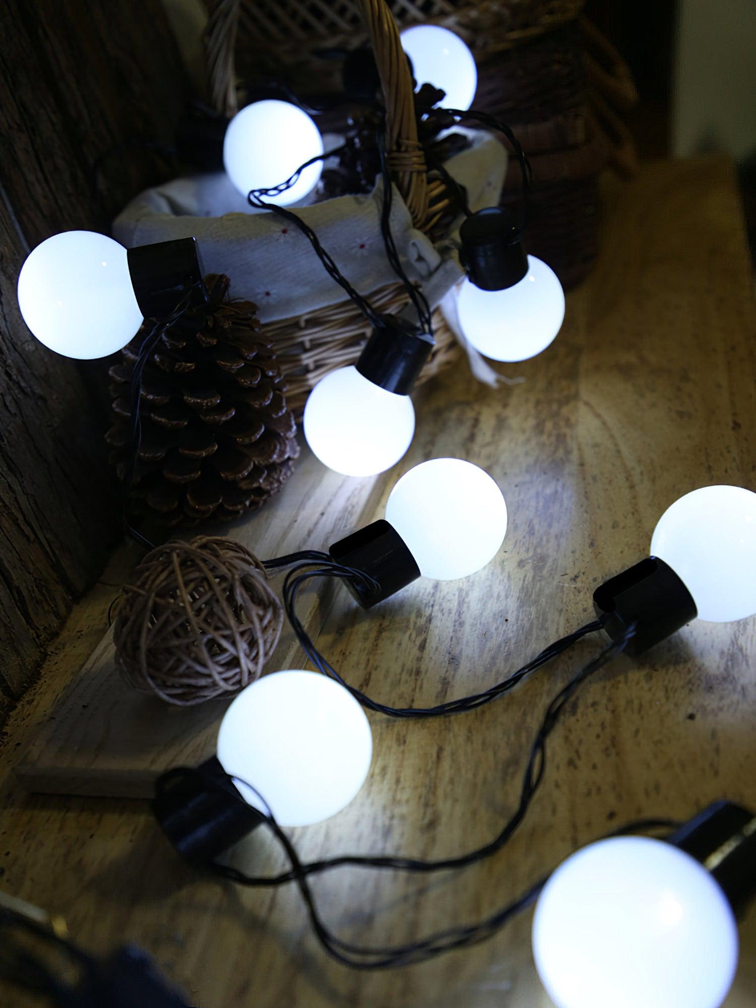 White globe lights and black wiring near pine cones