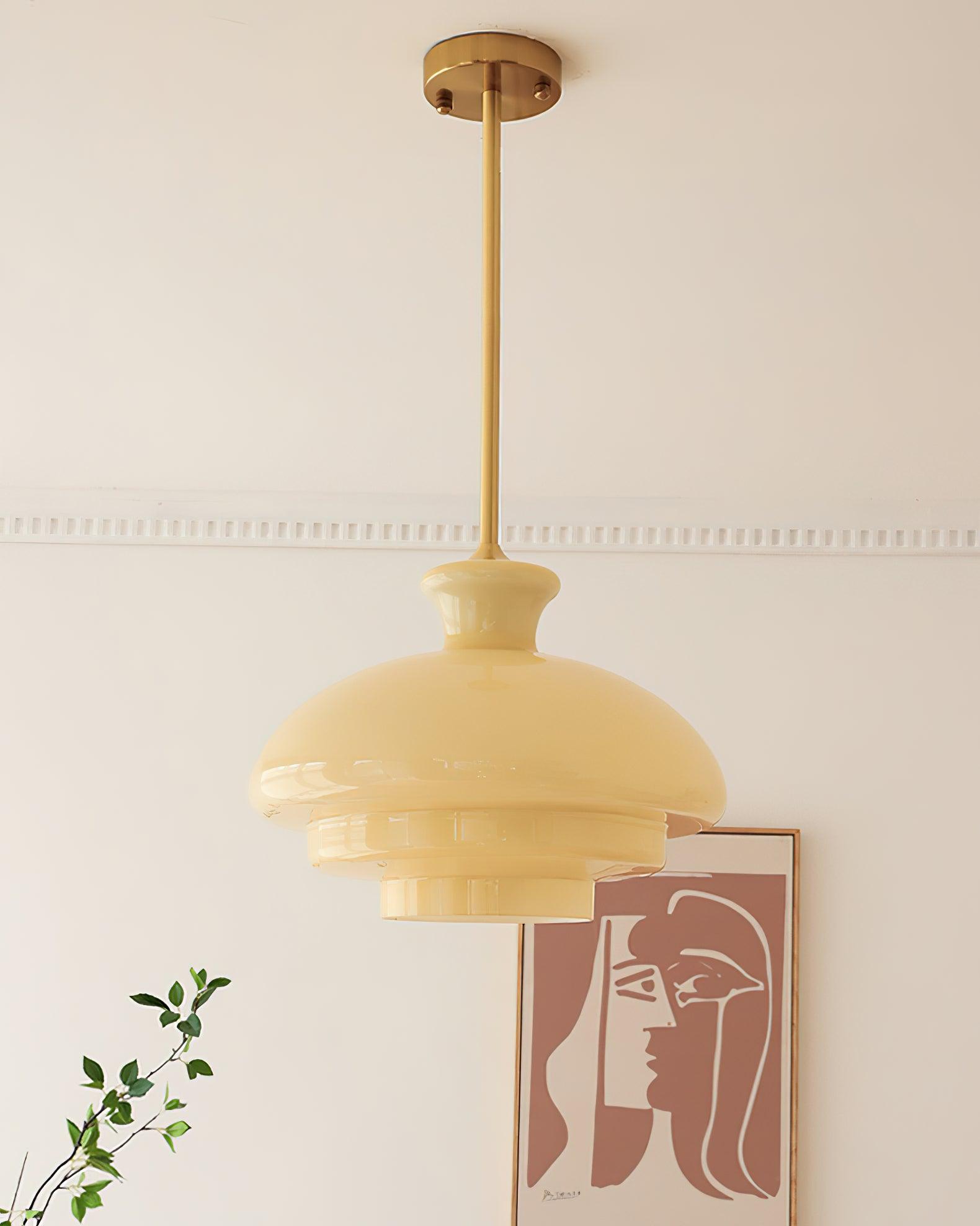 Full yellow glass pendant with gold-tone rod and round canopy against a pale wall with framed artwork