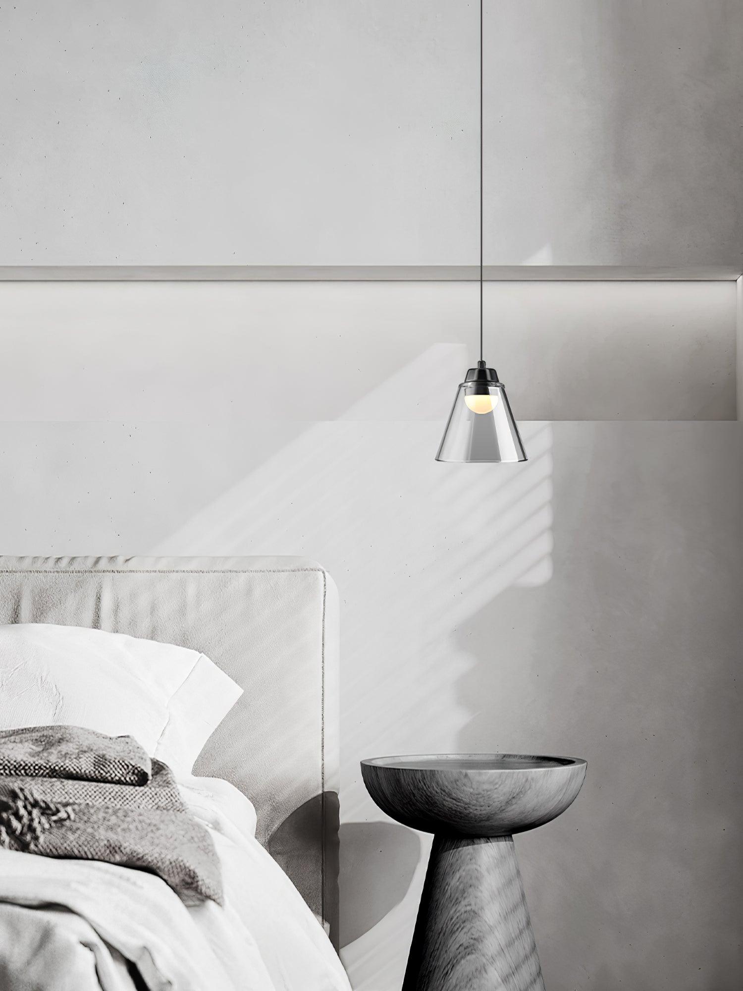Glass cone bedside pendant above a dark side table
