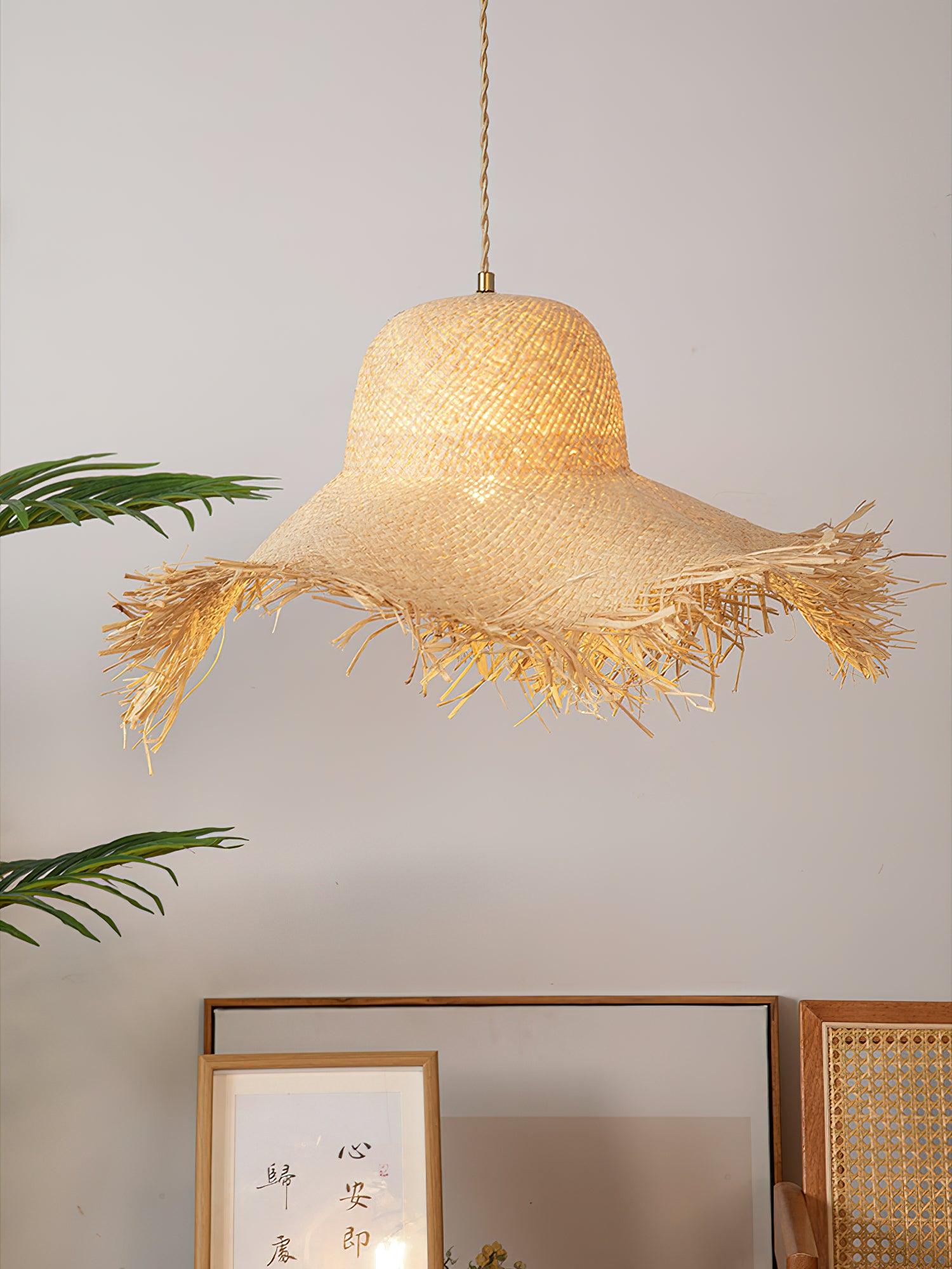 Warm-lit hat pendant over framed artwork and cane chair back, showing gold-tone top ferrule and tan cord