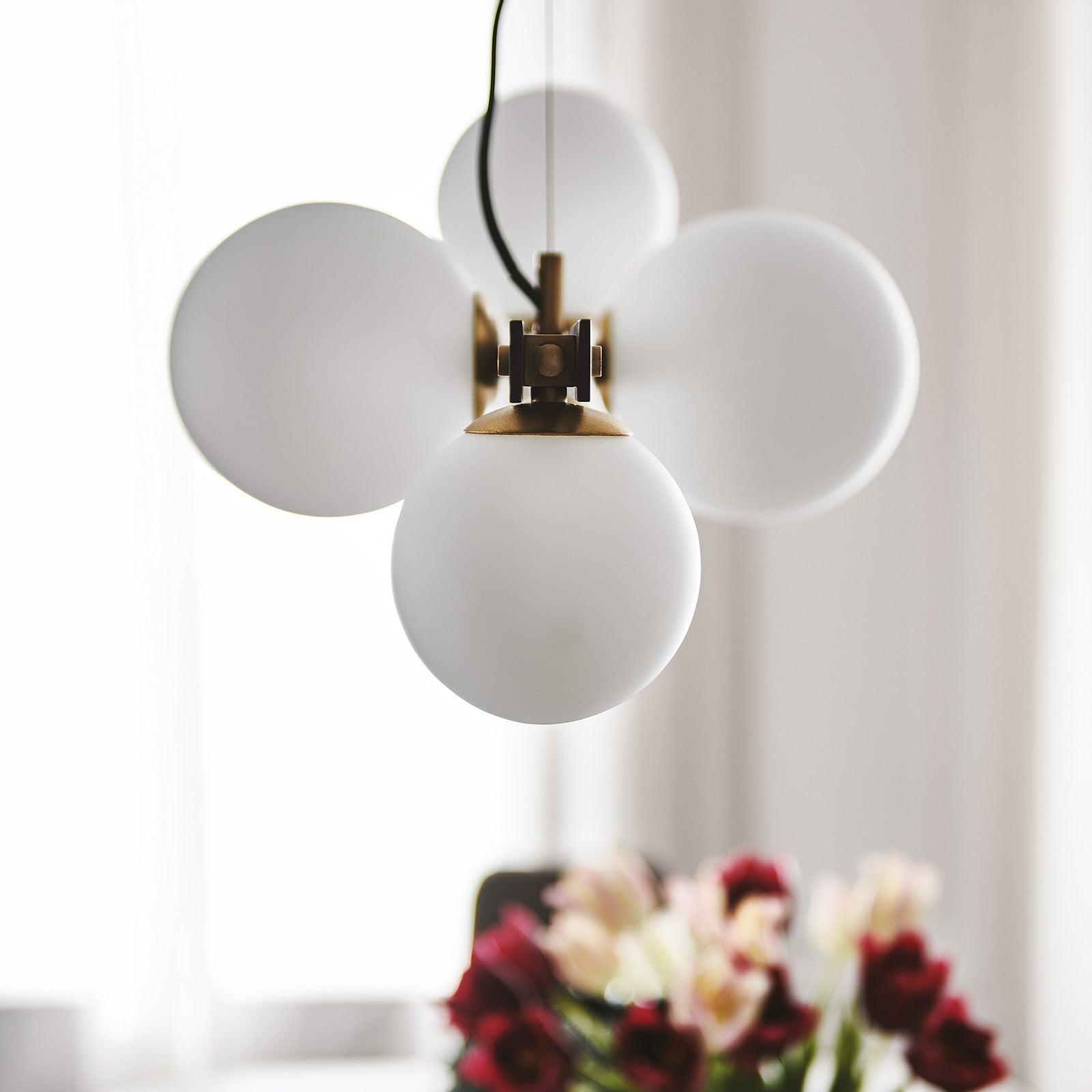 End-on close-up of white globes, brass-tone cup and fastener, black channel edges, dark power cord and fine support line.