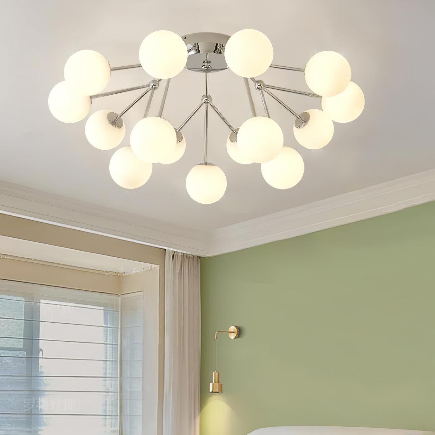 Lit chrome globe ceiling cluster in a bedroom with green wall, gold bedside wall light, window blinds and curtains