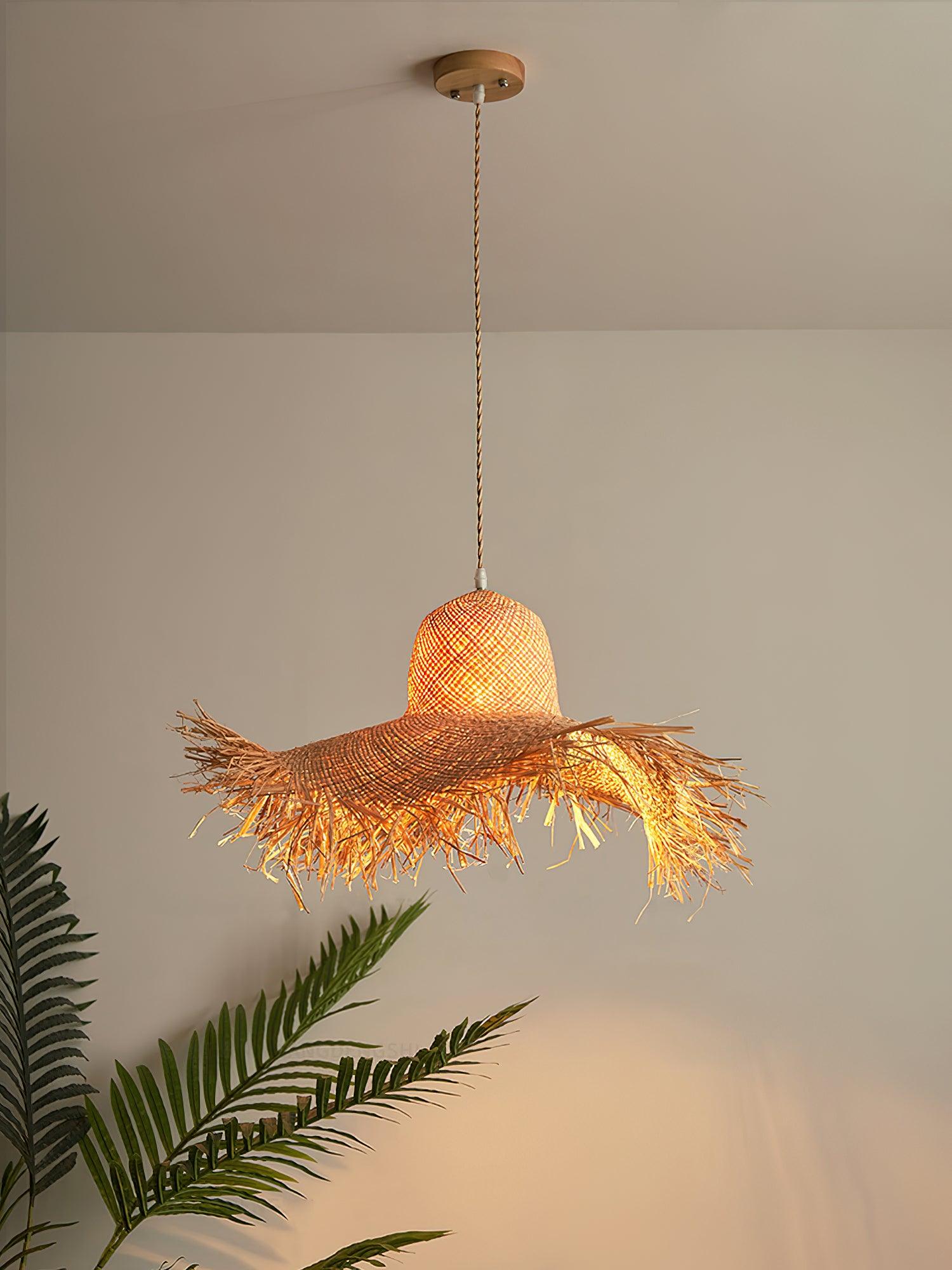 Full warm-lit hat pendant hanging from a round canopy on tan cord above palm fronds against a pale wall