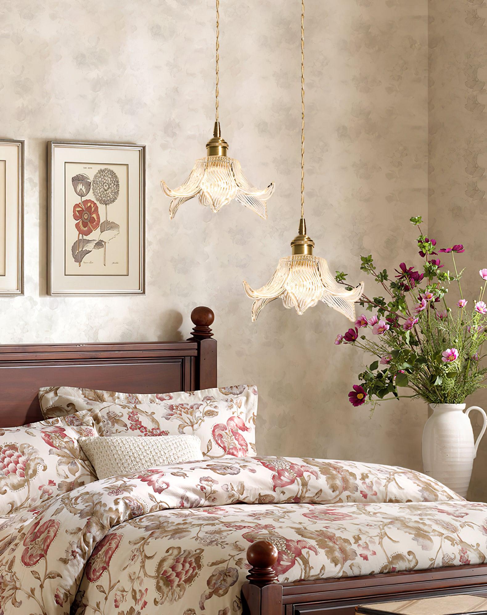 Two lit flower glass pendants at different heights beside a dark wooden bed, floral bedding, botanical prints and purple flowers in a white jug.