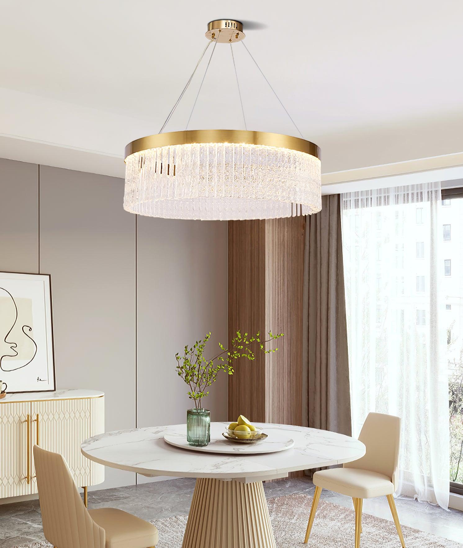 Clear-panel ring over round stone-pattern dining table with fluted base, cream chairs, green vase and fruit bowl