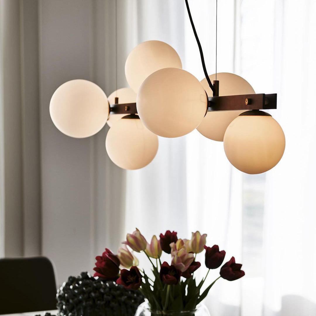Close end-angle view of glowing globes around black bar and brass-tone fittings, beside sheer curtains with tulips below.