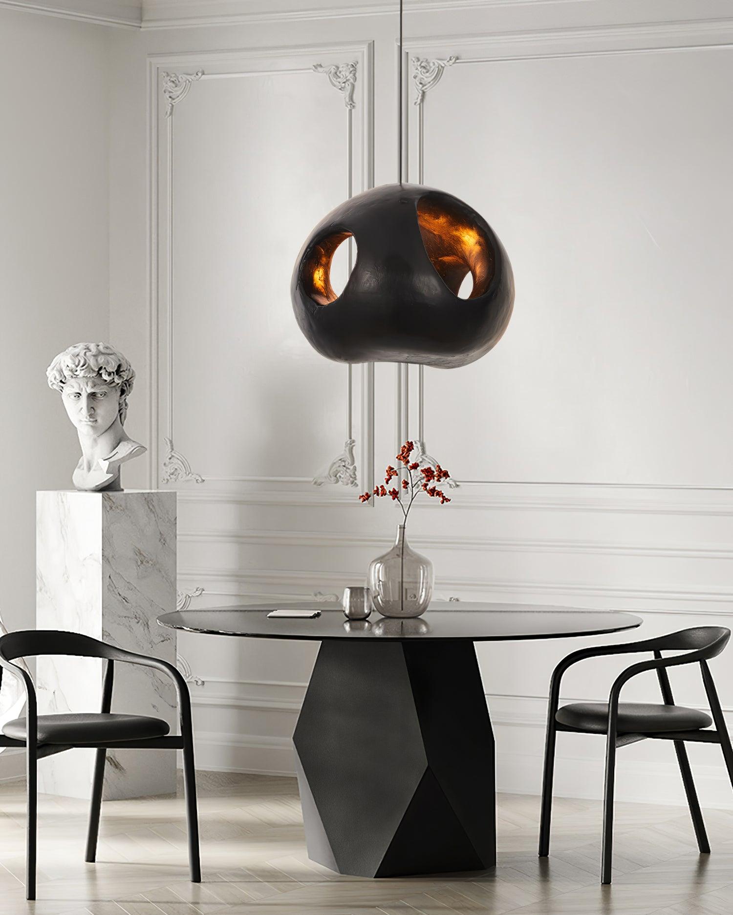Black cutout pendant above a dark dining table and black chairs, with a glass vase of red branches and a white bust beside it