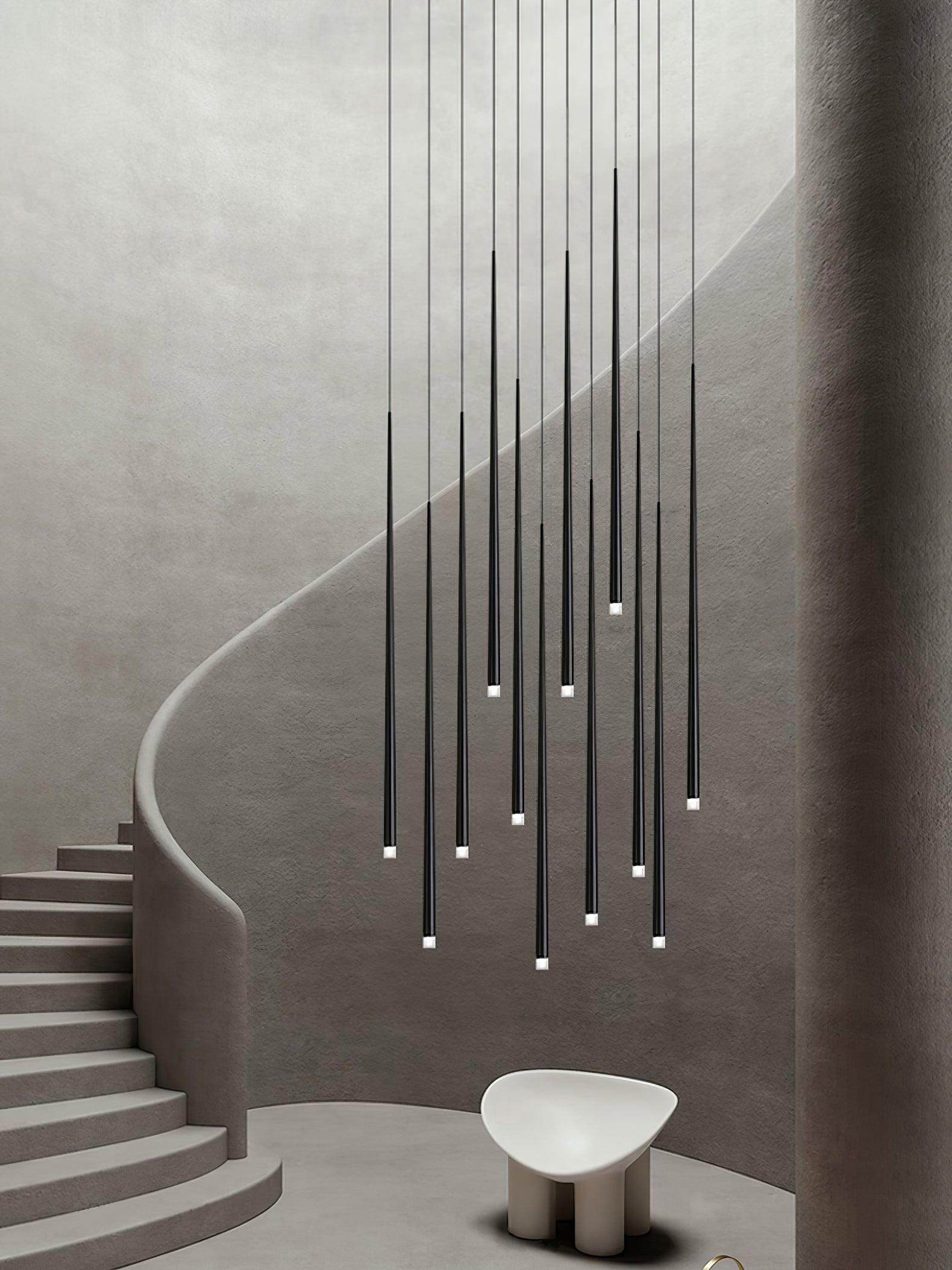 Slender Cone tube cluster beside a curved grey staircase and white chair in a tall interior