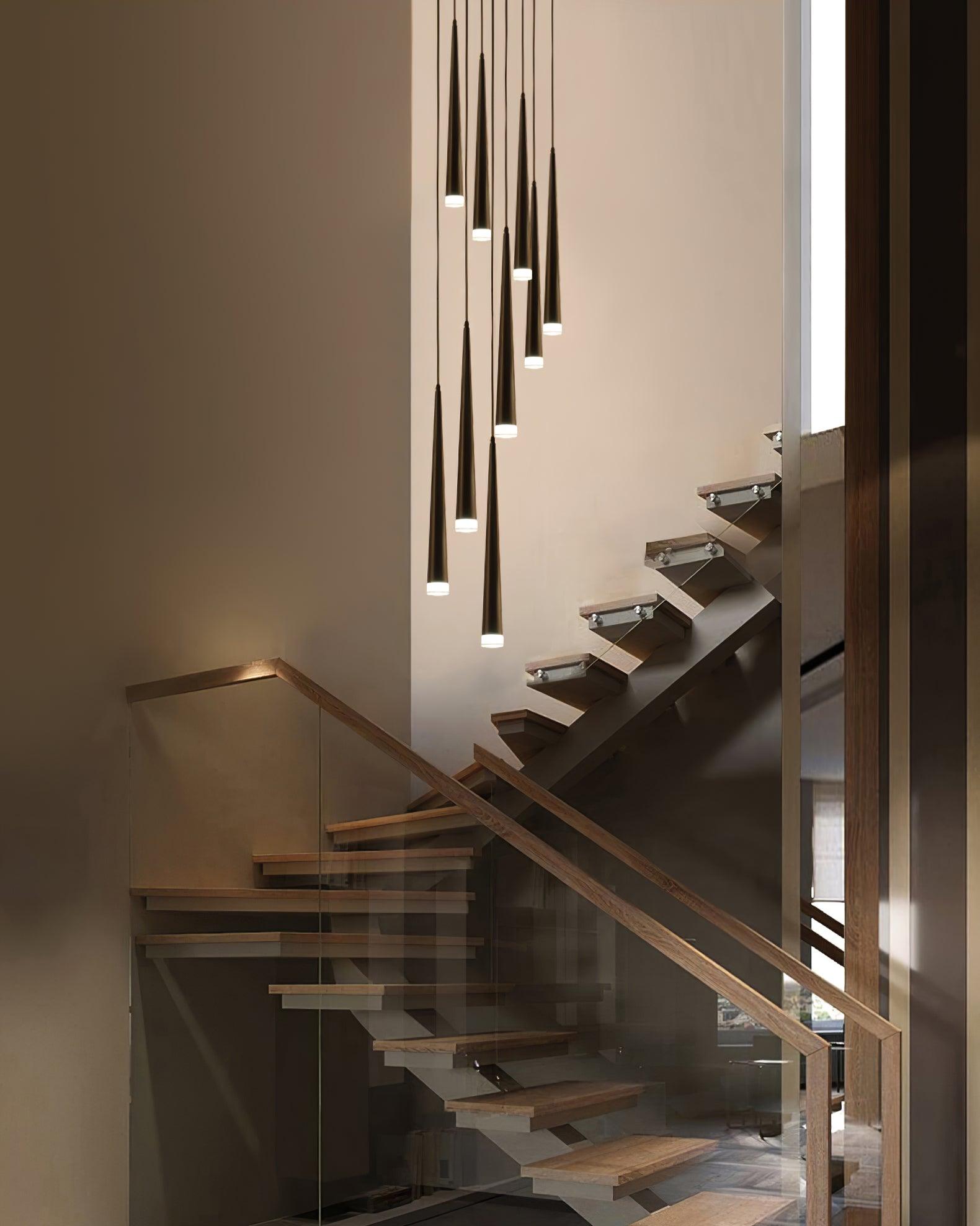 Black tapered pendant cluster descending beside wooden stairs and a glass balustrade