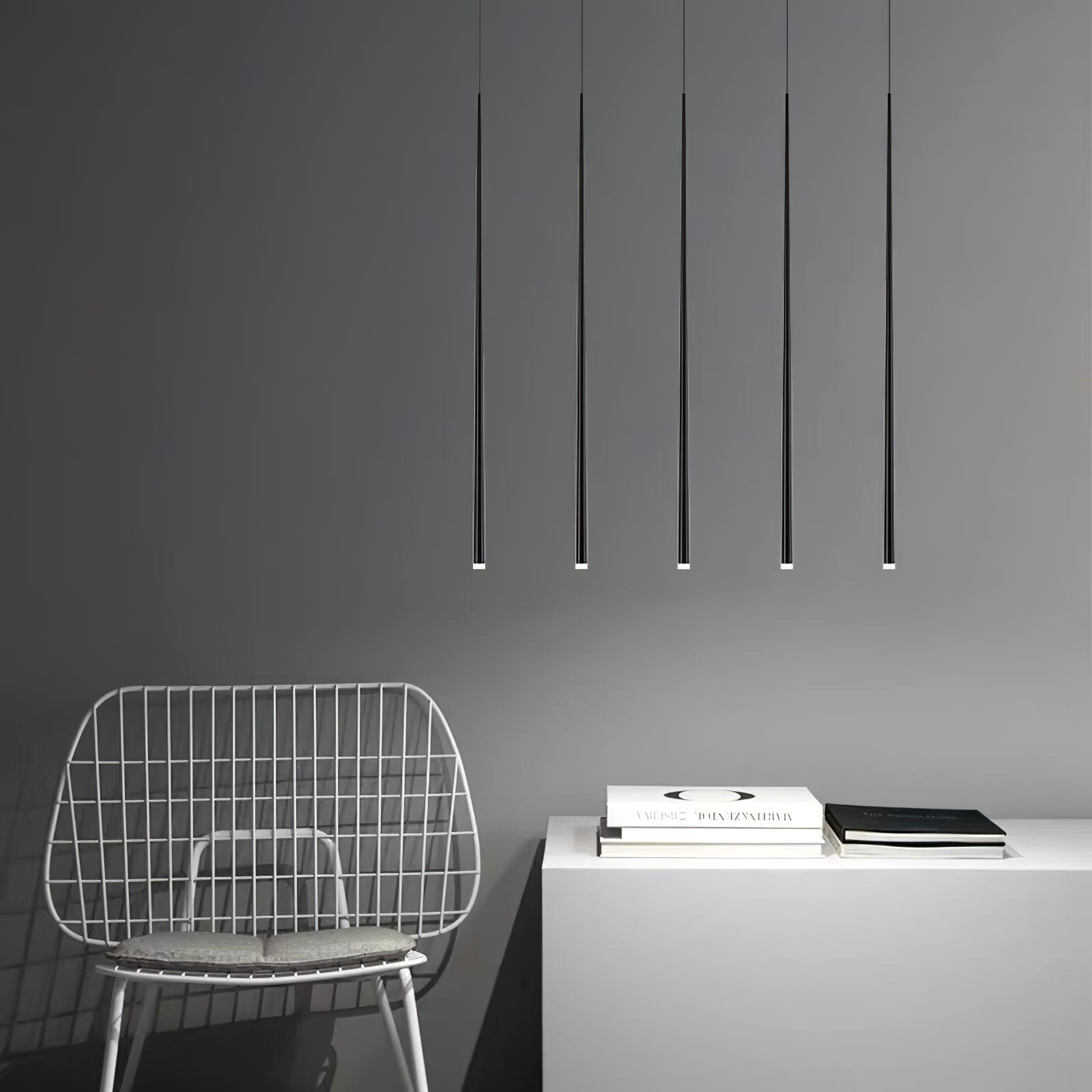 Five black tapered pendant tubes above a white console with books beside a wire chair