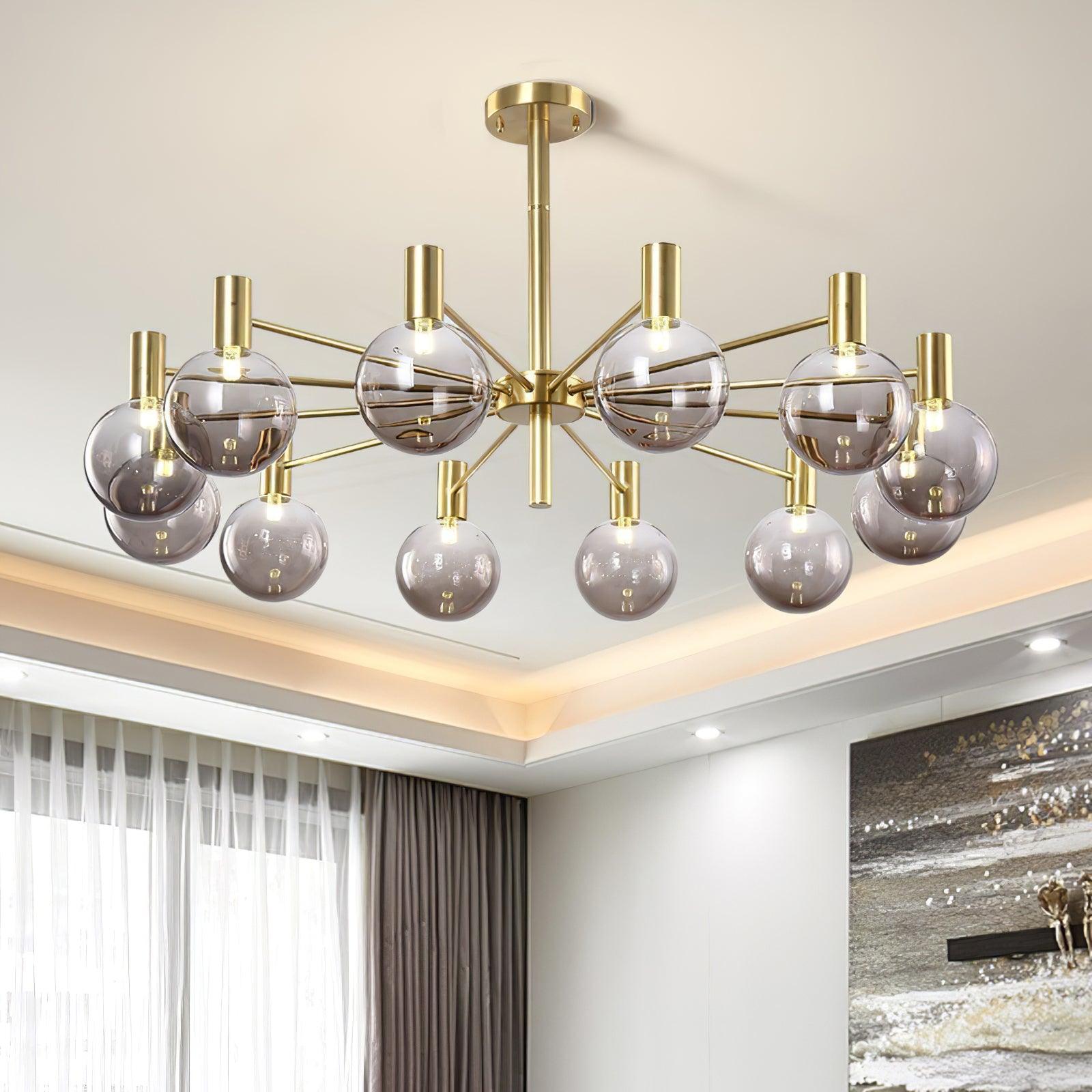 Upward view of twelve lit clear globes on gold-tone arms beneath a cove-lit ceiling, beside curtains and wall art.