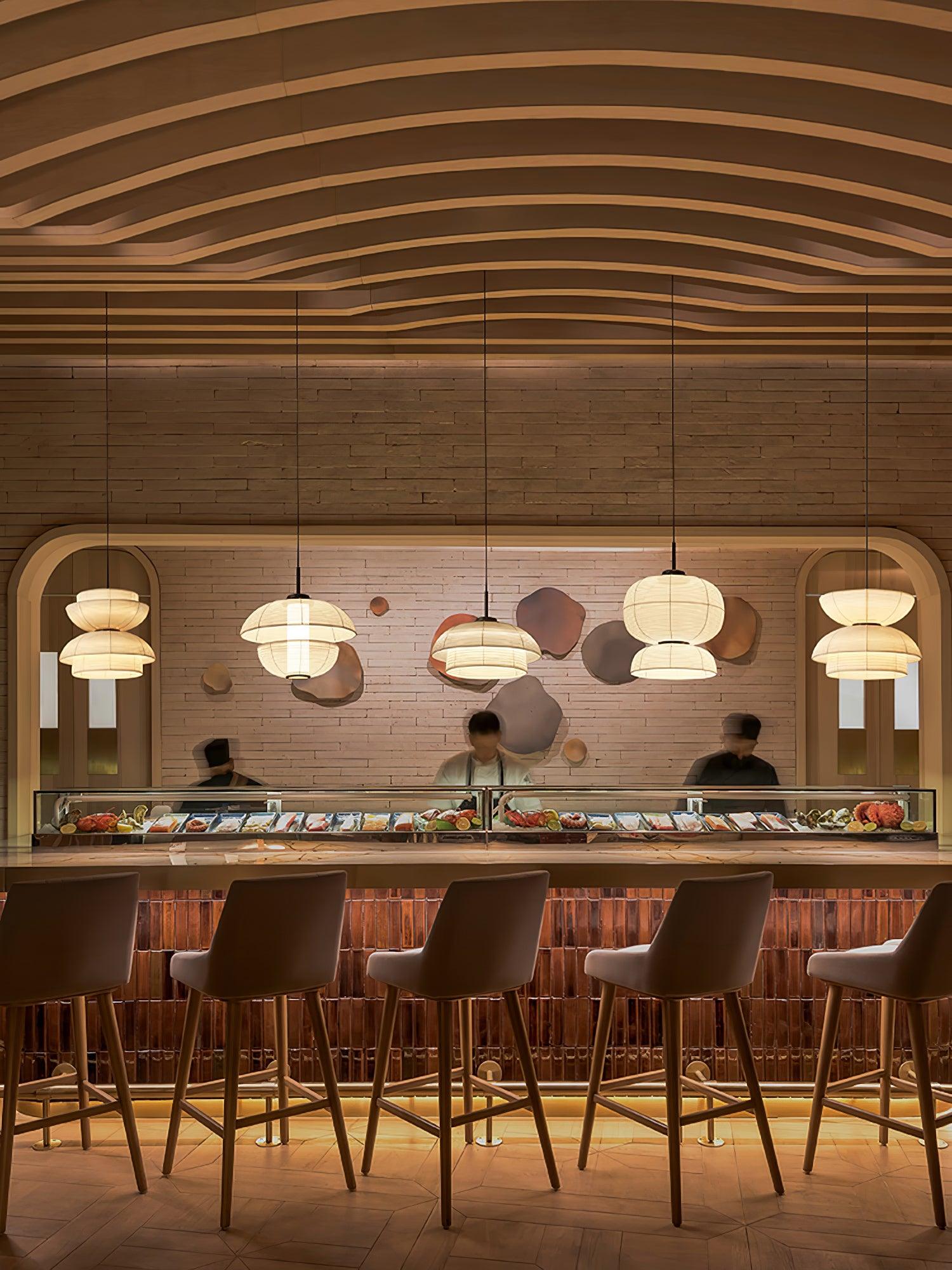 Portrait of five separate fabric pendants in different shapes along a restaurant counter with barstools