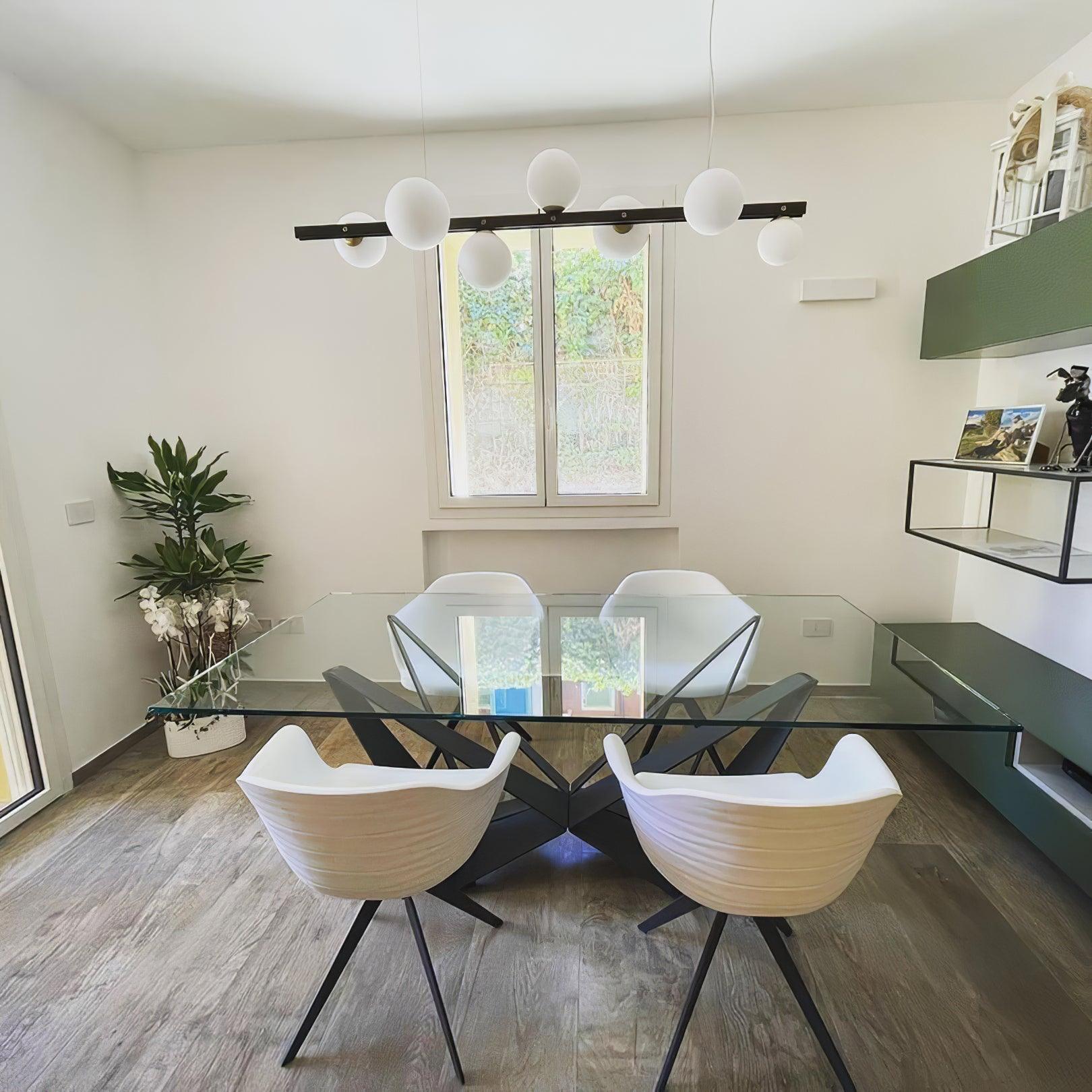 Globe pendant over square glass table and four white chairs, with small window, potted plant and dark green shelving.