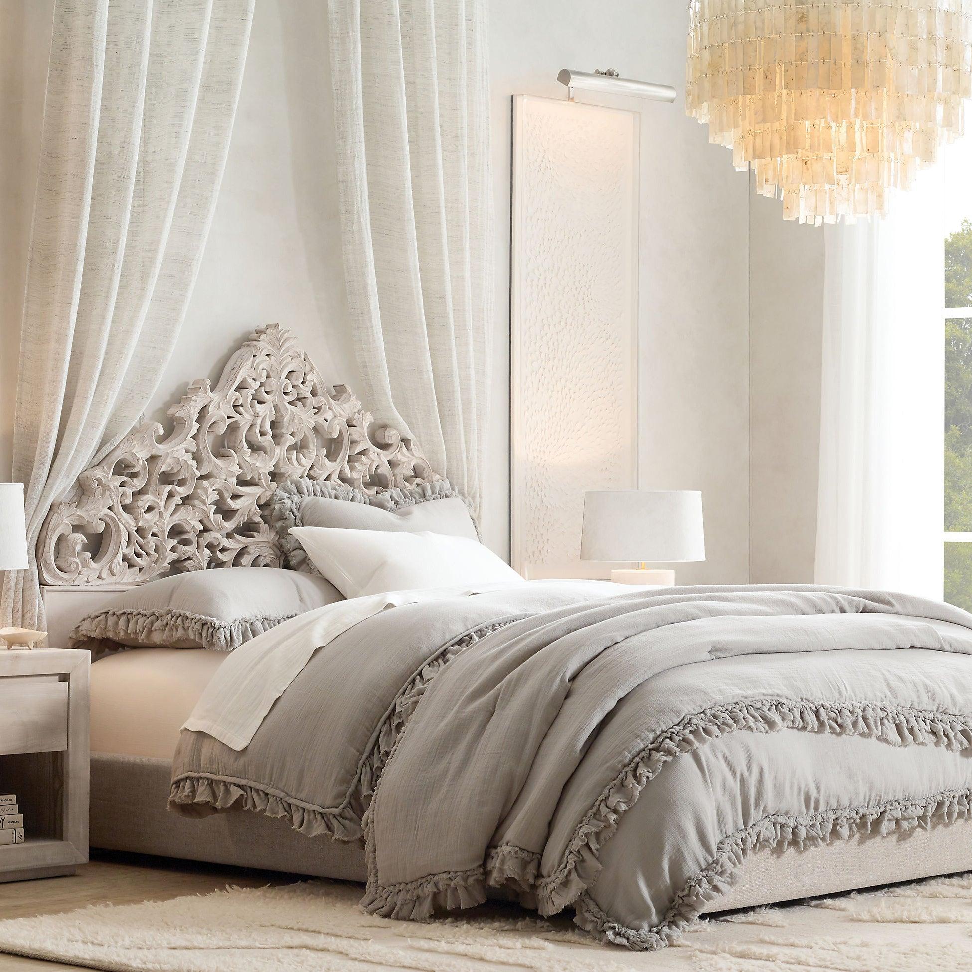 Cropped shell pendant above grey bedding and a carved white headboard, with white curtains and bedside table lamps