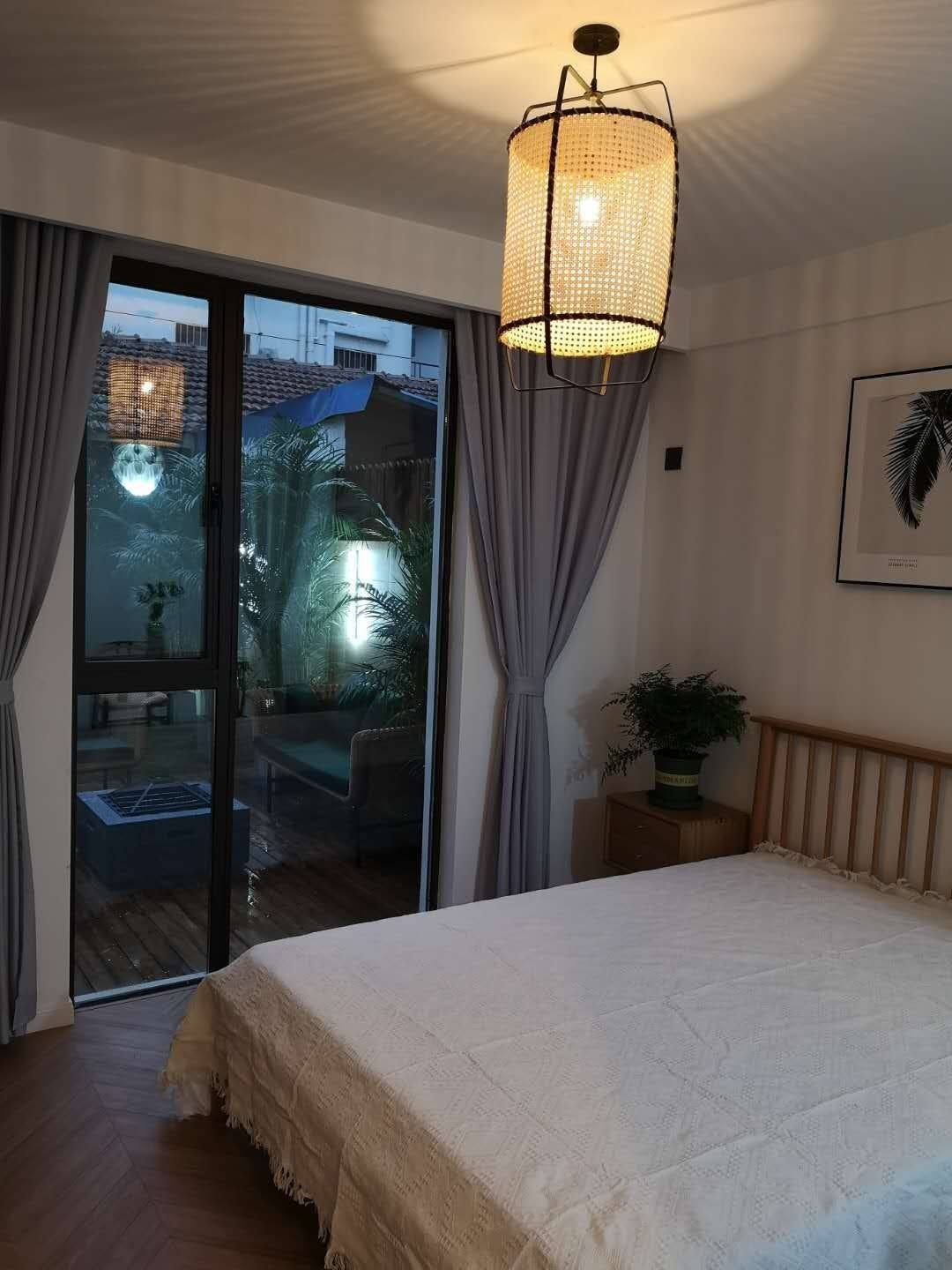 Glowing cane pendant in a bedroom with wooden headboard, grey curtains and glass doors