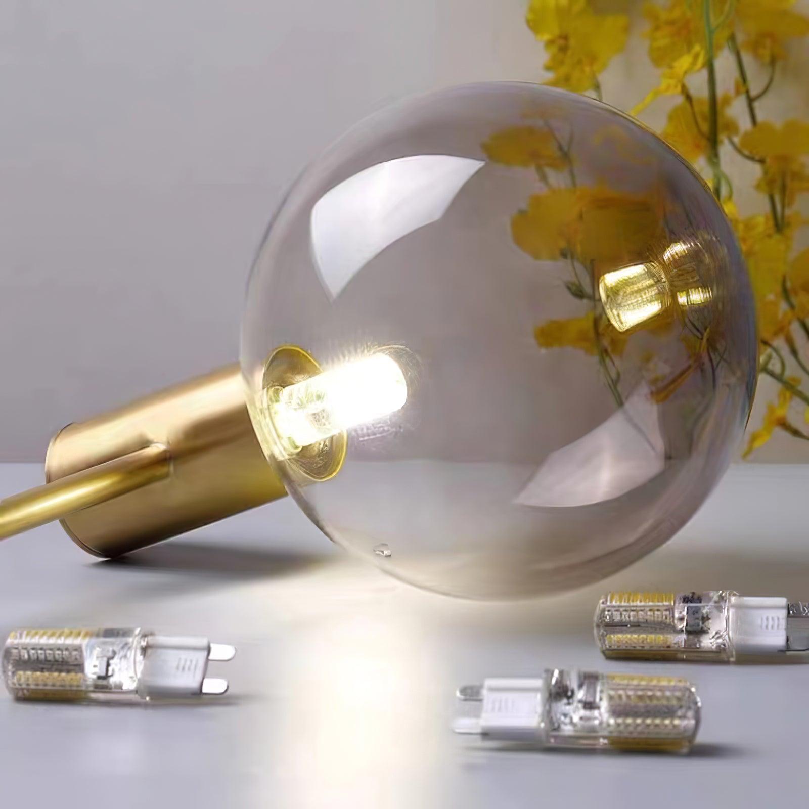Clear globe and gold-tone holder resting sideways with a lit capsule lamp inside and three loose loop-pin bulbs nearby.