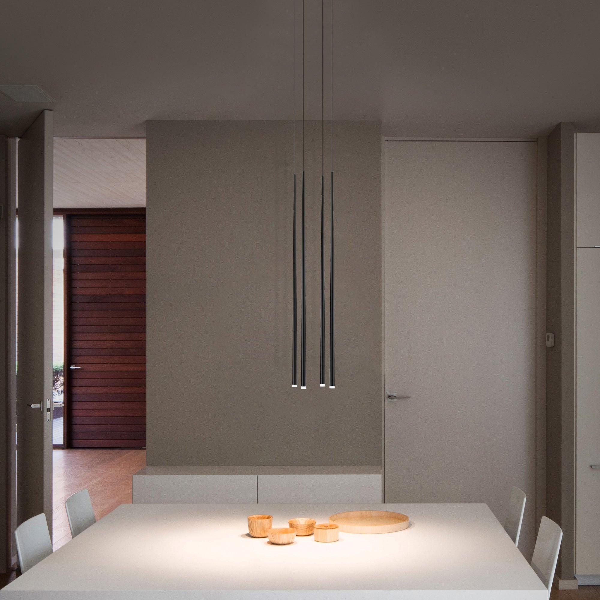Four black tubes on long cables over a white dining table with wooden bowls in a grey room