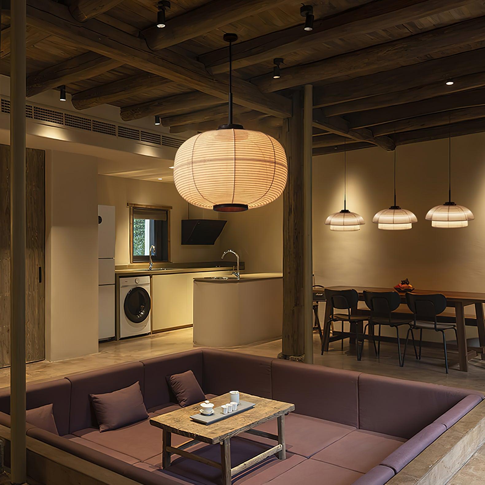 Oval fabric pendant over a seating area, with three dome-and-collar pendants over a dining table beside a kitchen