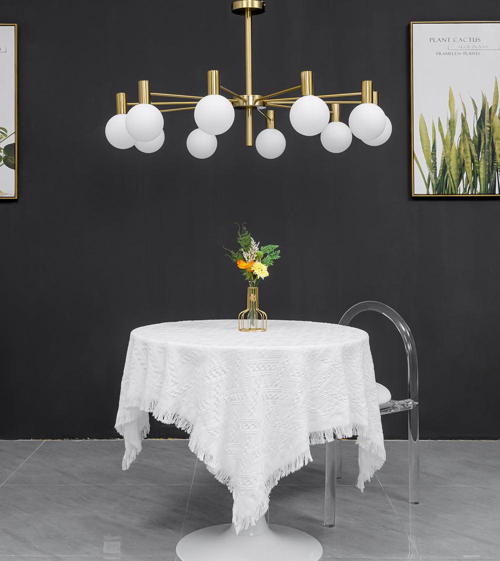 Front view of an unlit white-globe chandelier above a round cloth-covered table between two botanical prints.