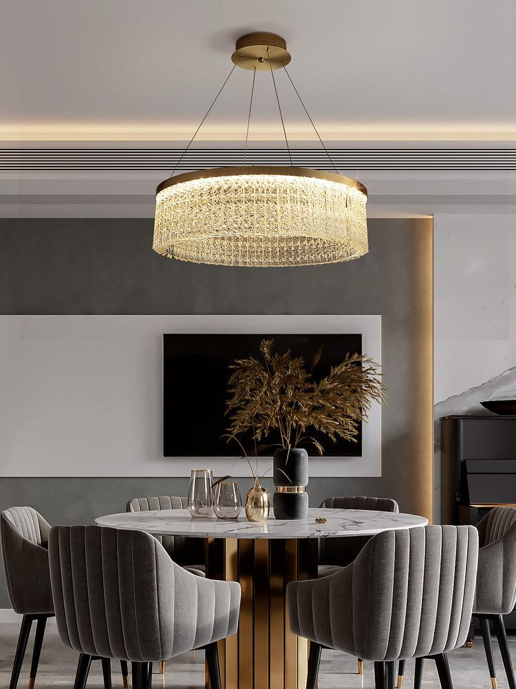Full crystal ring chandelier above round pale dining table, grey upholstered chairs, metal vessels and dried branches