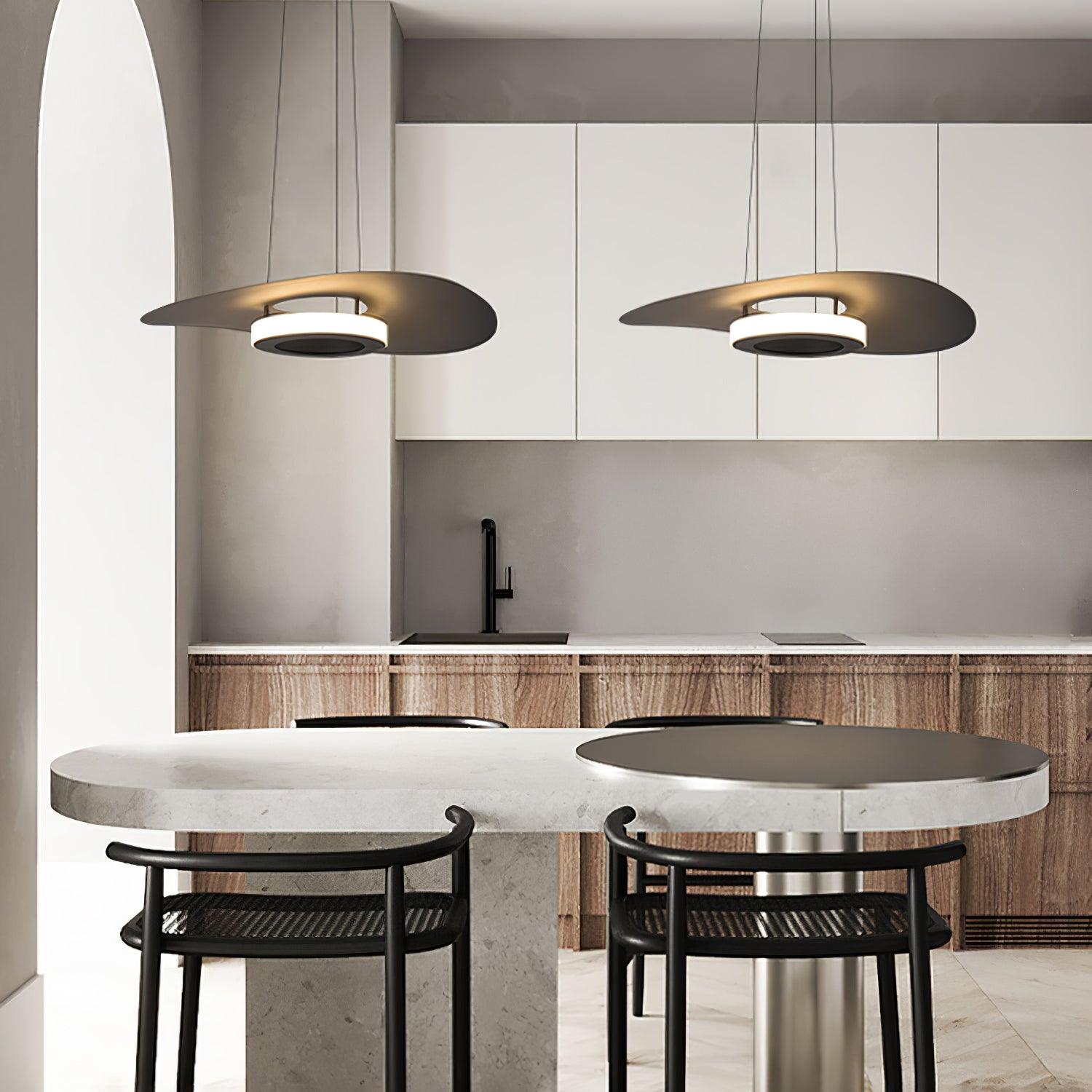 Two dark disc pendants above rounded stone kitchen island table with black stools and white cabinets