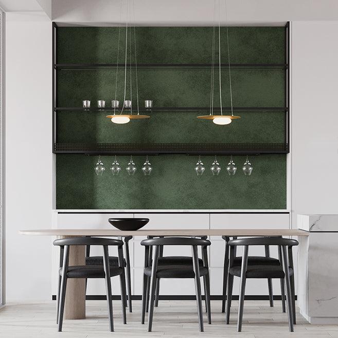 Front view of two gold pendants above a pale table and black bowl, with a wide wine-glass rack against a green wall.