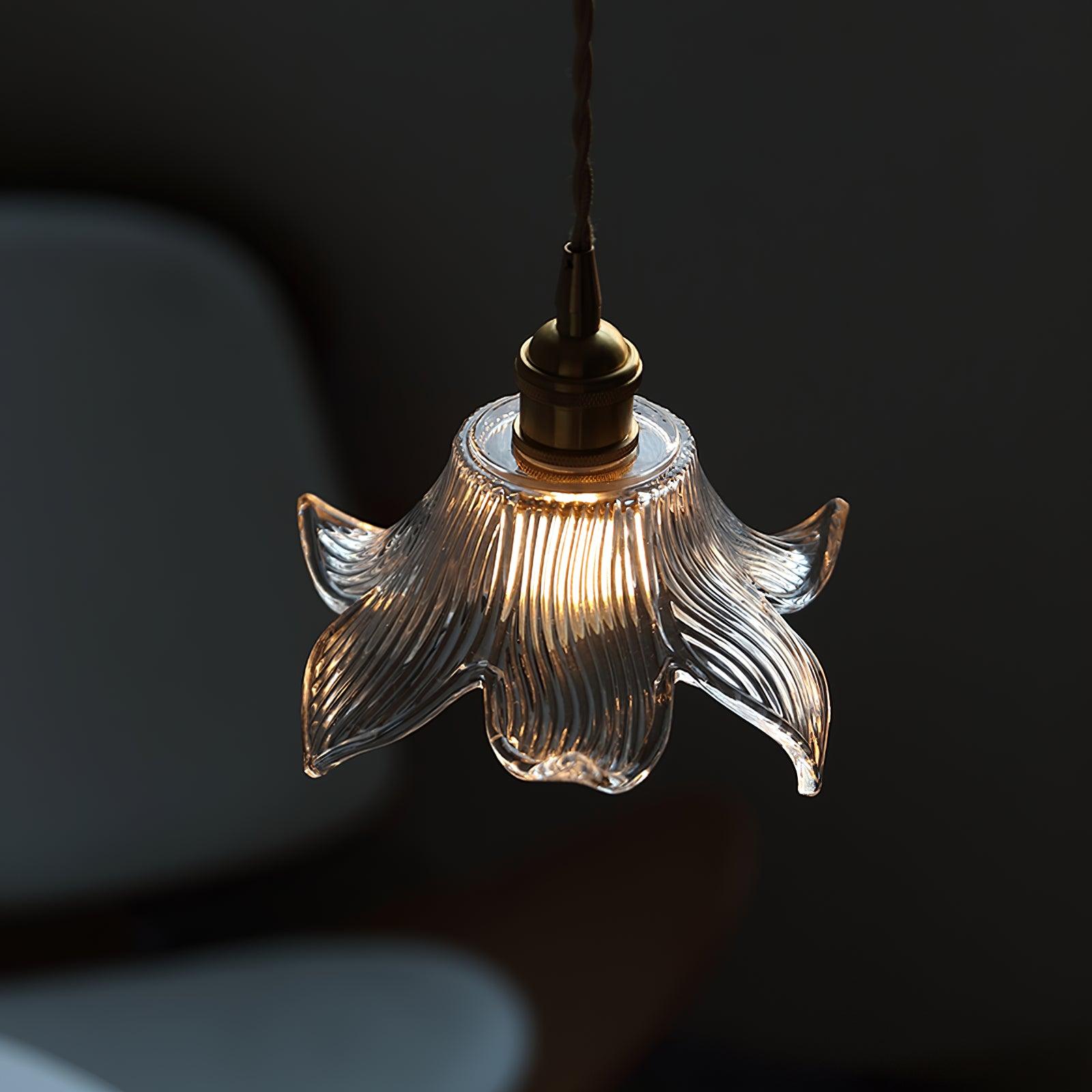 Close illuminated glass shade with curved ribs and pointed curling petals beneath a brass-toned holder on grey.