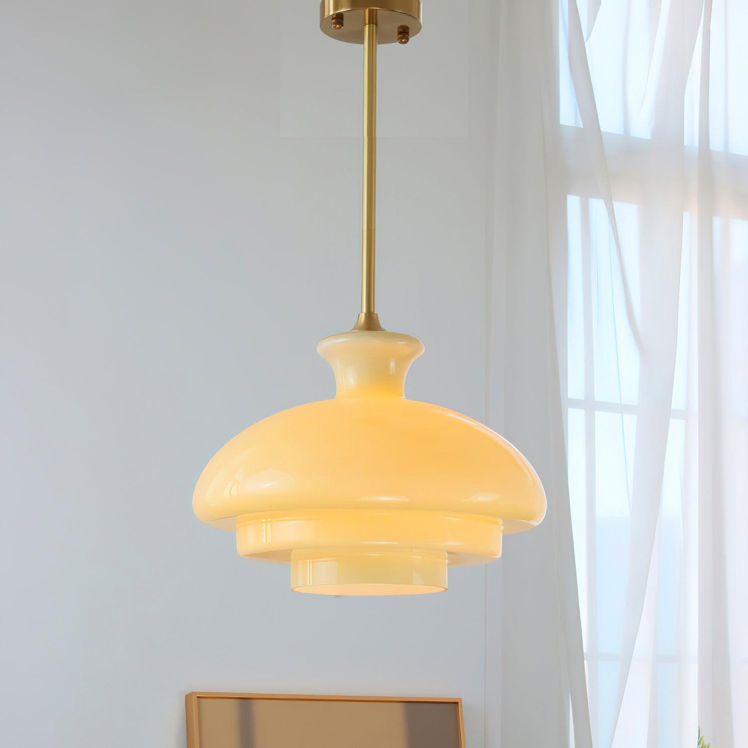 Yellow stepped glass pendant on a gold-tone rod and round canopy beside white curtains and a window